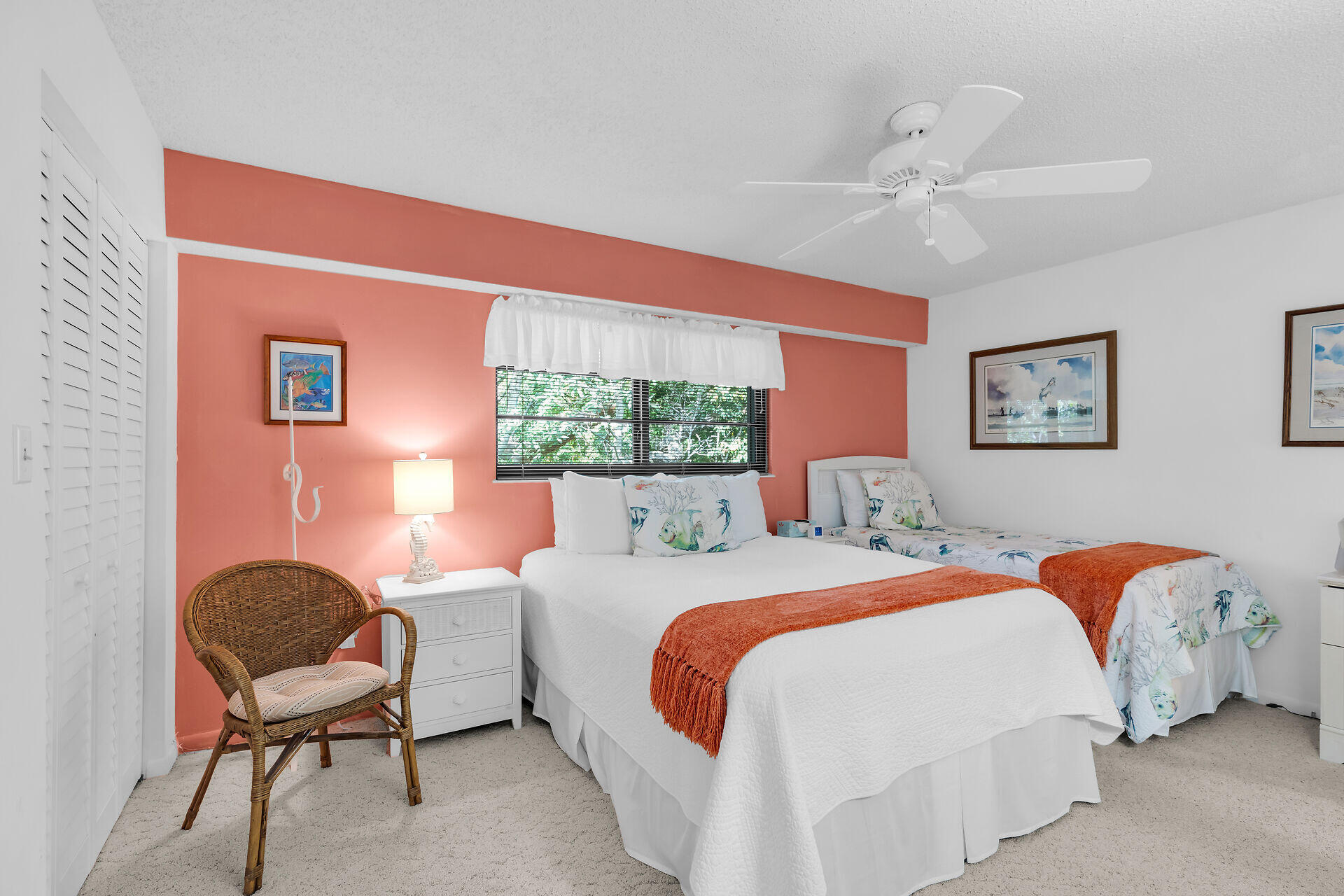 Bedroom with two beds, fish-print bedding, orange throws, and a coral accent wall.