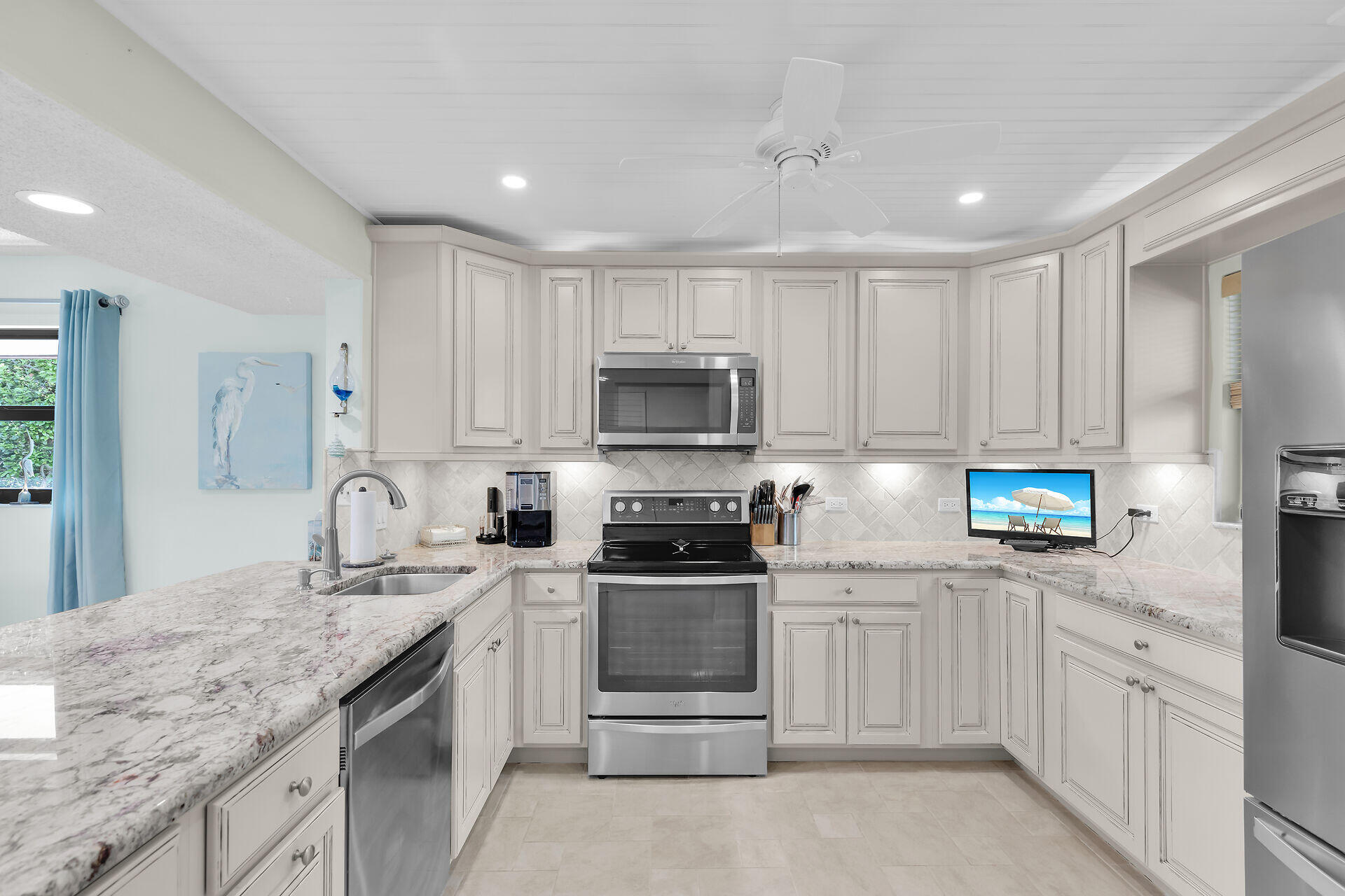Kitchen with white cabinetry, granite counters, stainless appliances, and blue curtains by the sink.