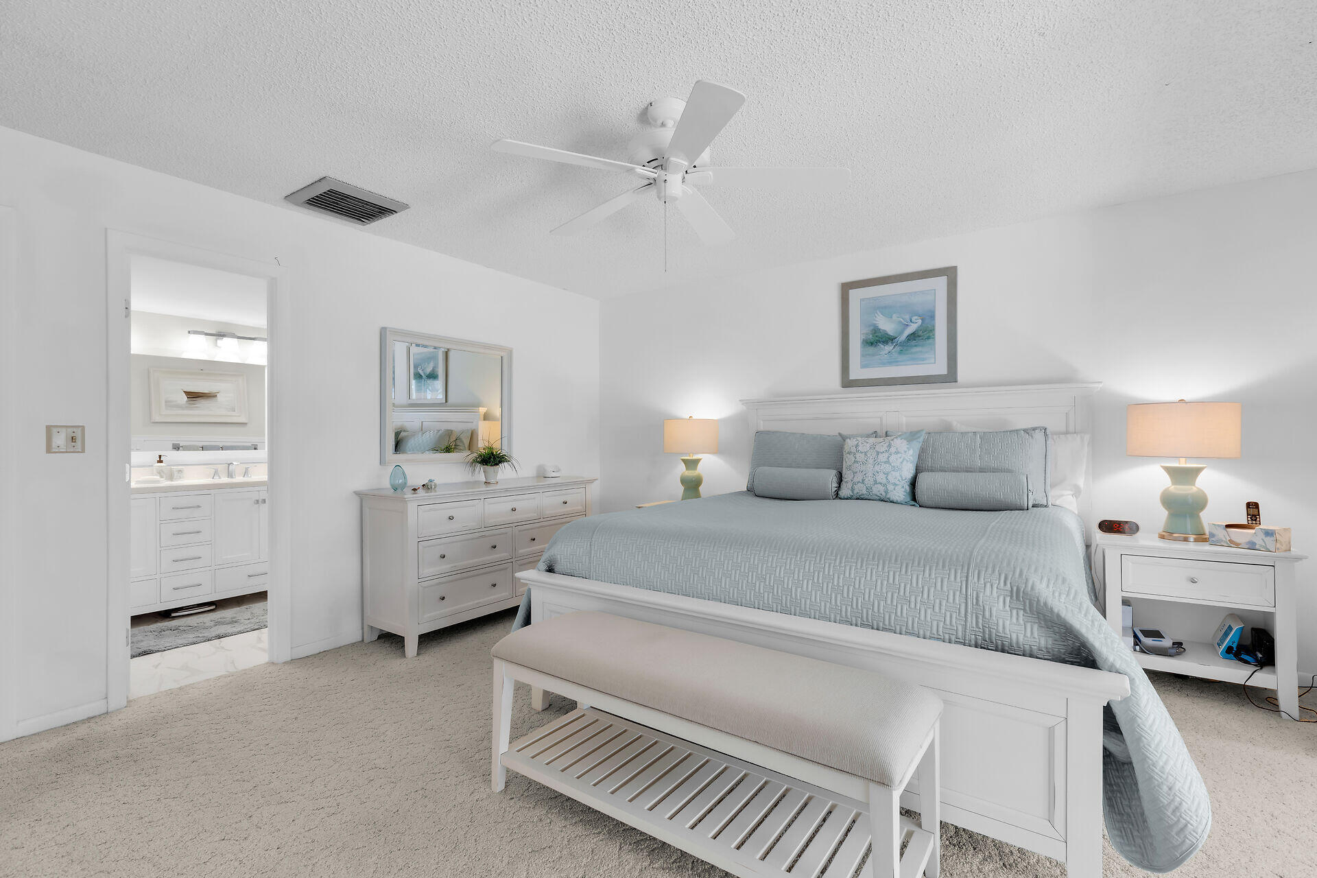 Bright bedroom with pale blue bedding, white furnishings, and an ensuite bathroom doorway.