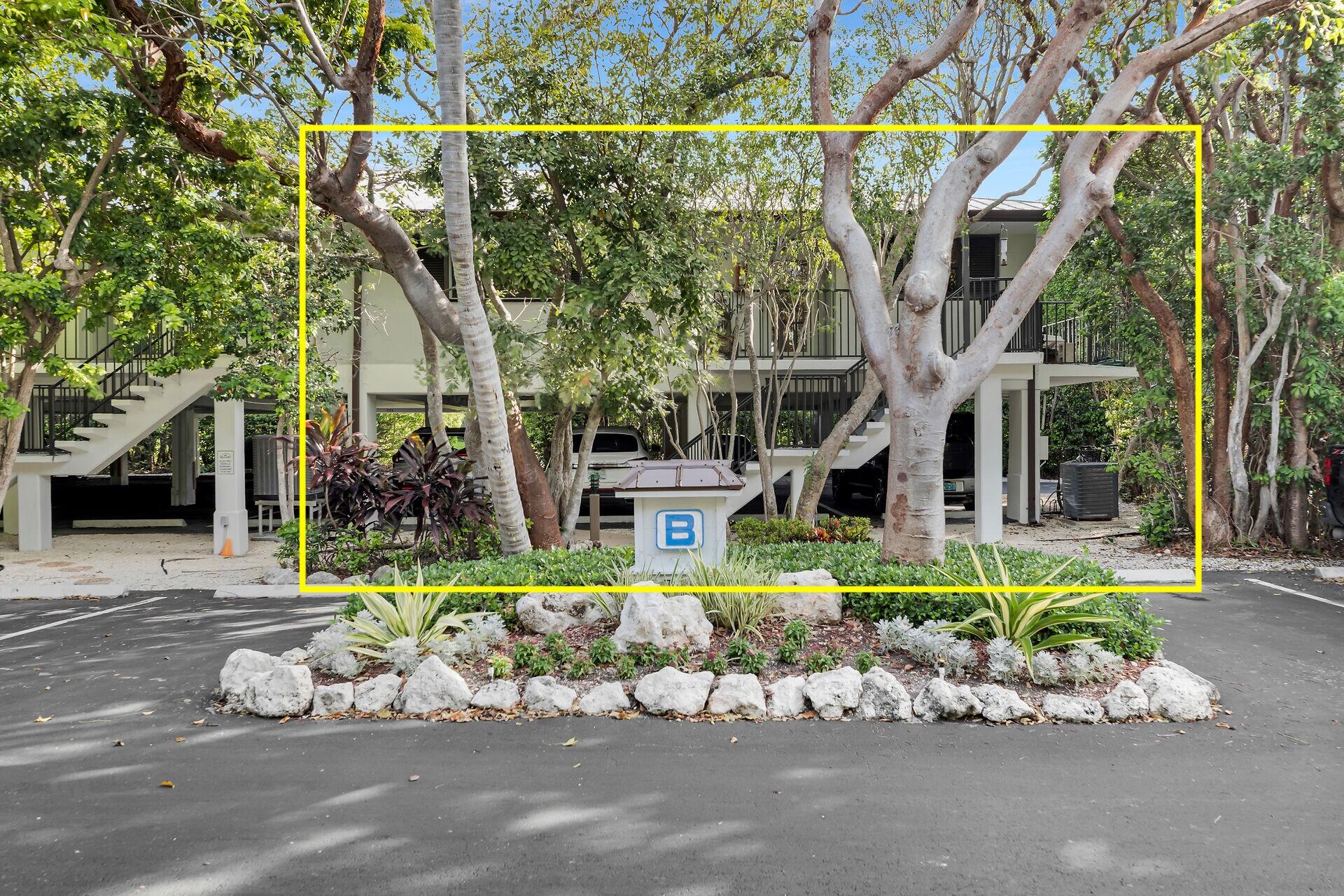 Elevated residence surrounded by tropical trees, with a landscaped entrance and a pedestal marked B.