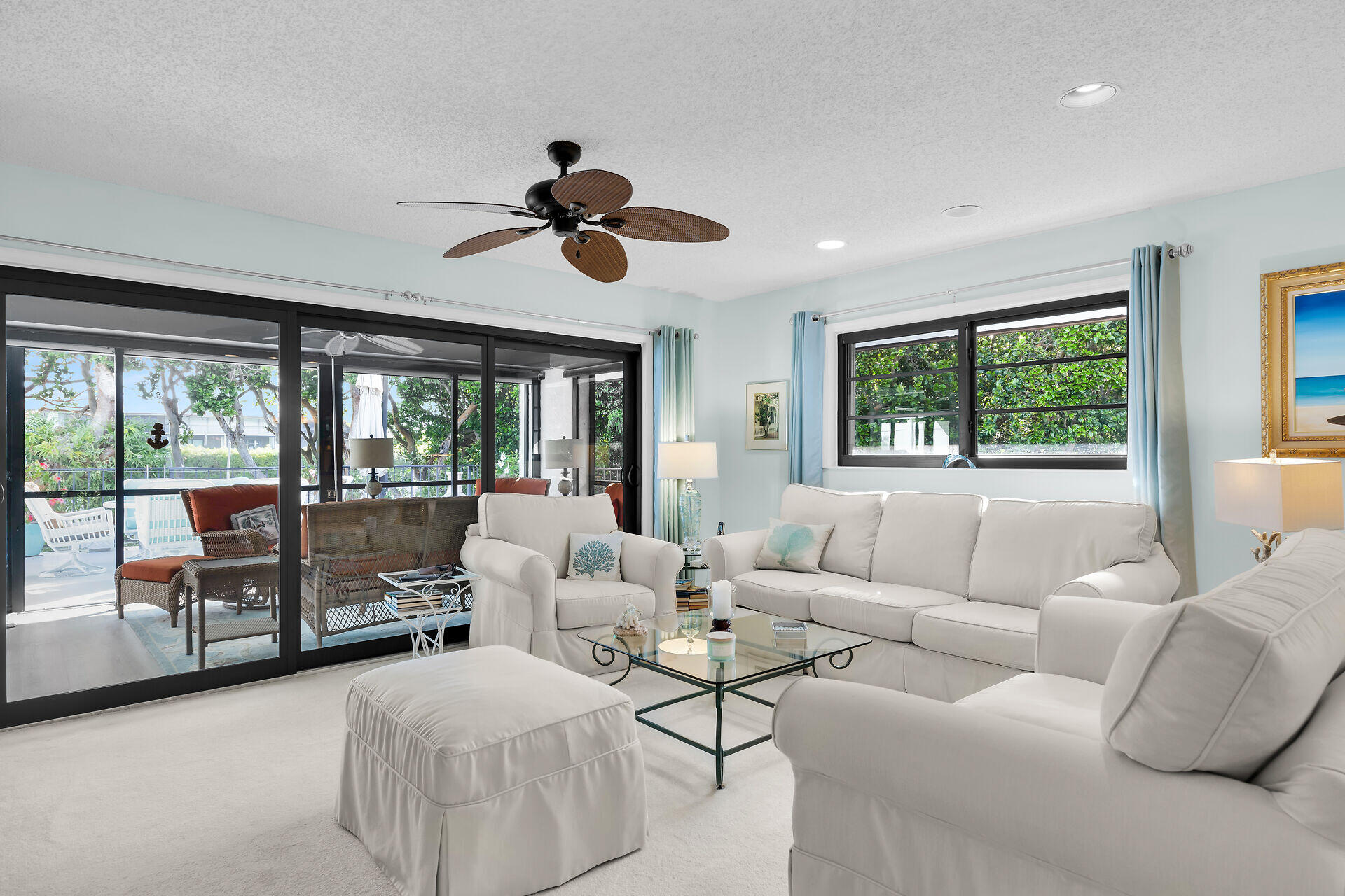 Furnished living room with white sofas and sliding doors opening onto a leafy patio.