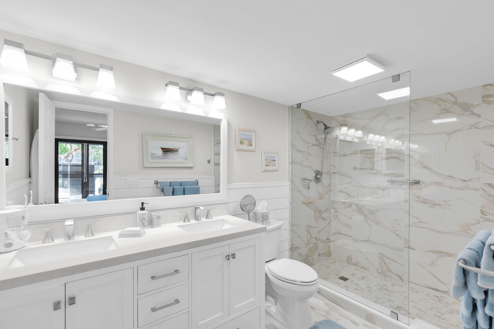 Bright bathroom with a white double vanity and a glass-enclosed marble-look shower.