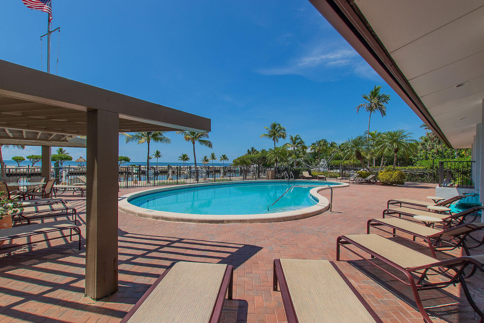 Outdoor pool deck with lounge chairs, palm trees, and water beyond.