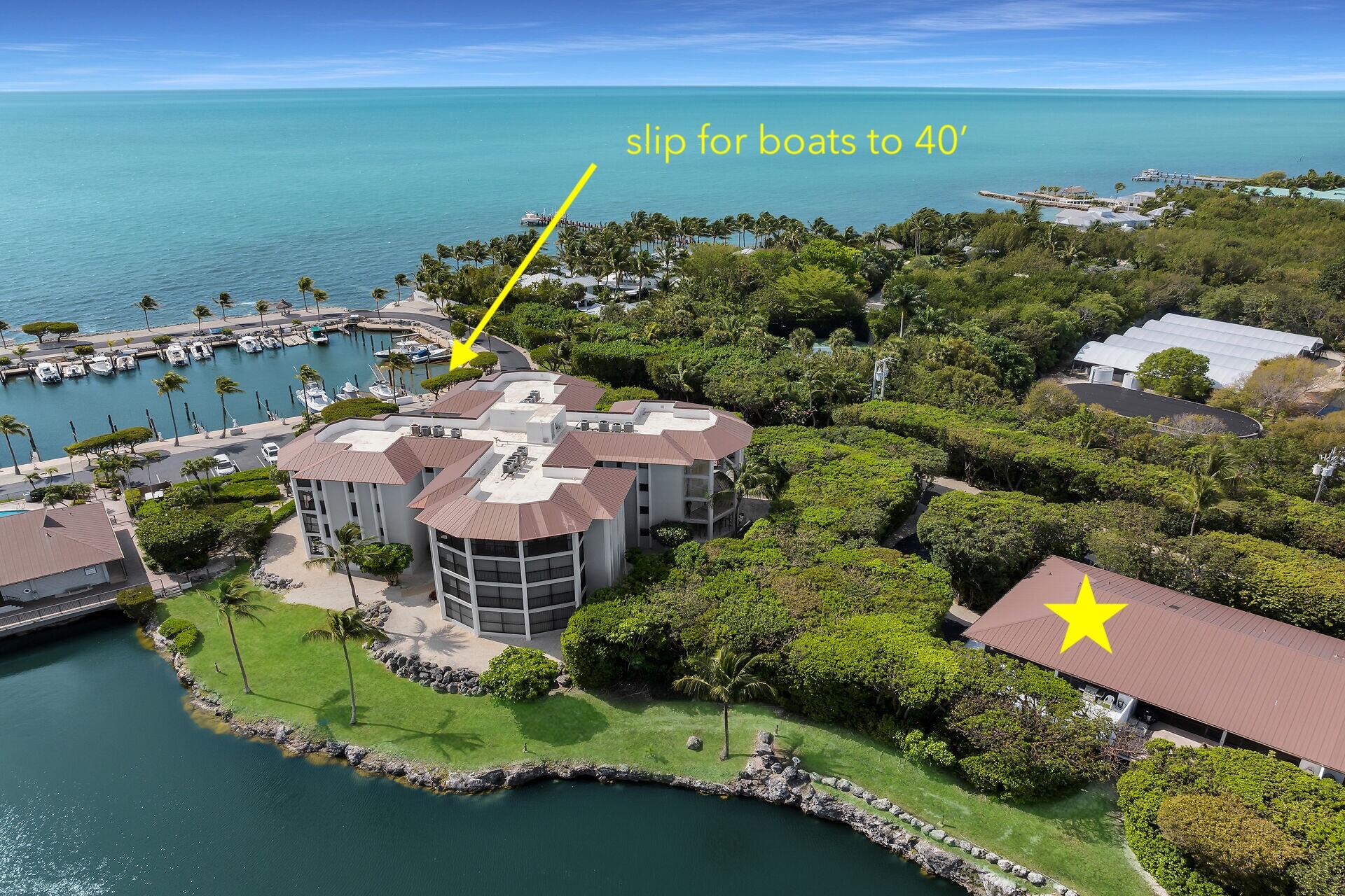 Aerial view of a waterfront condominium with a marked boat slip and marina beside turquoise water.