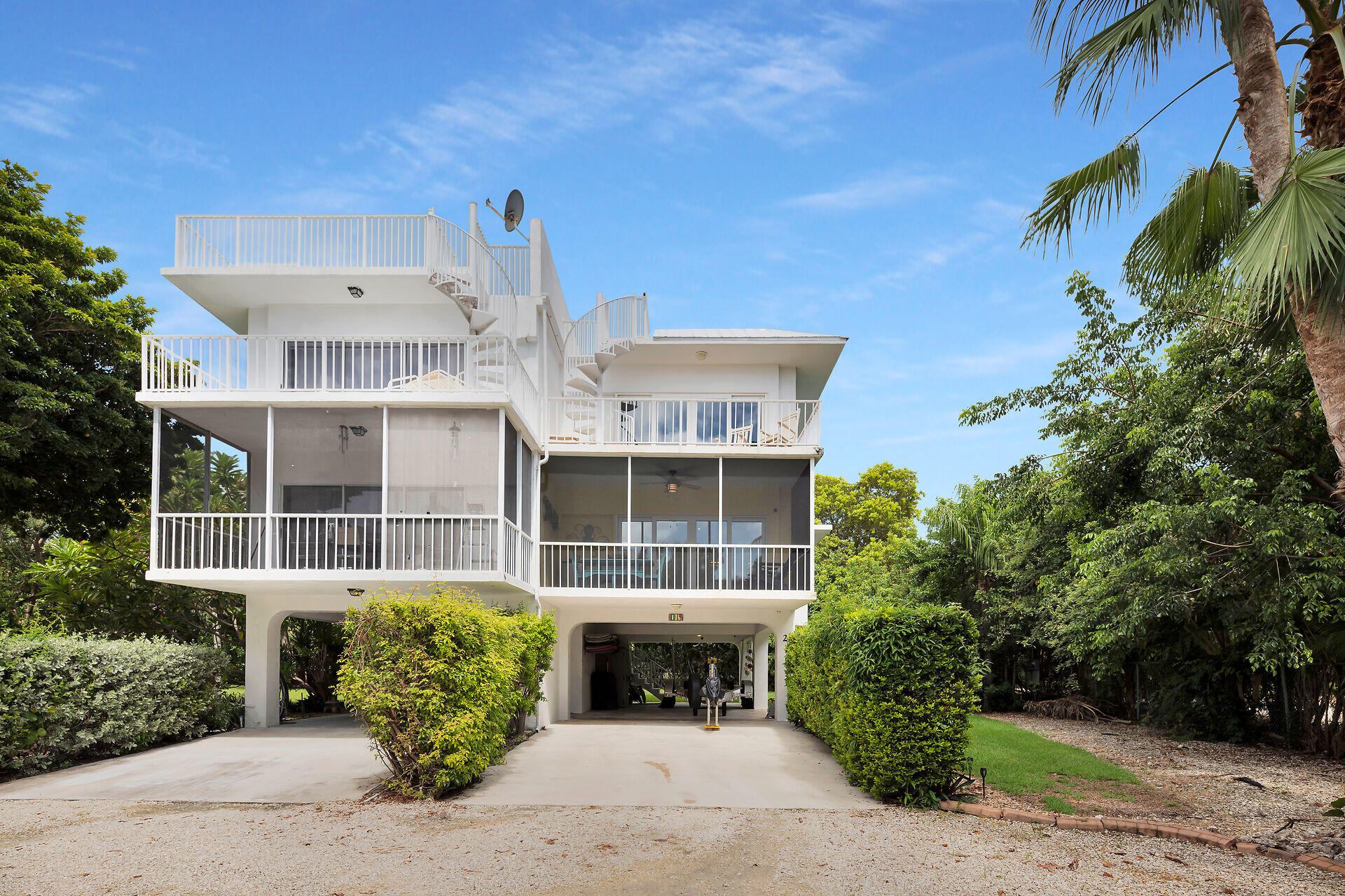 Elevated white home with multiple balconies and a rooftop deck amid tropical landscaping.