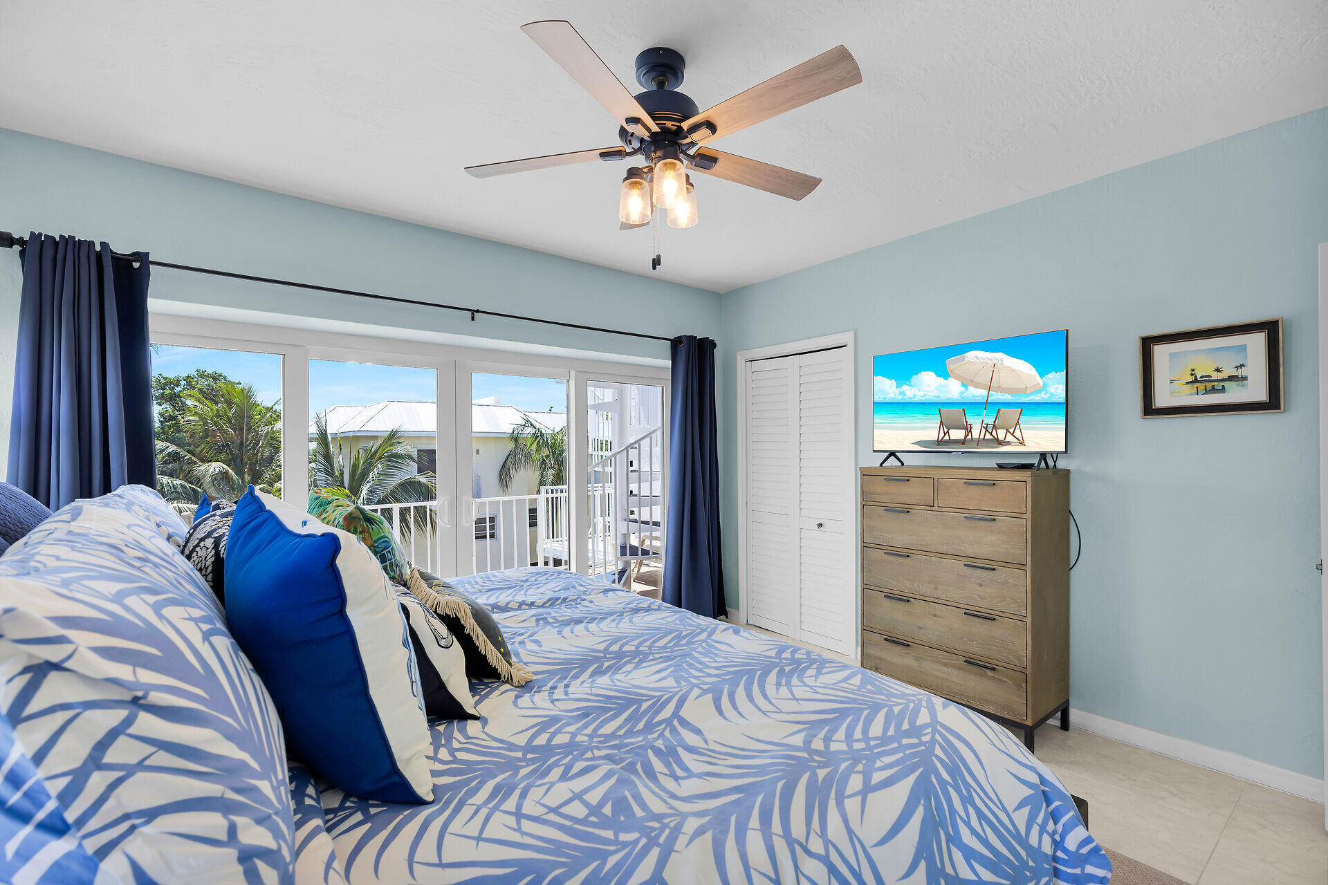 Bedroom with blue-and-white bedding, blue accent pillows, and sliding glass doors opening to a balcony.