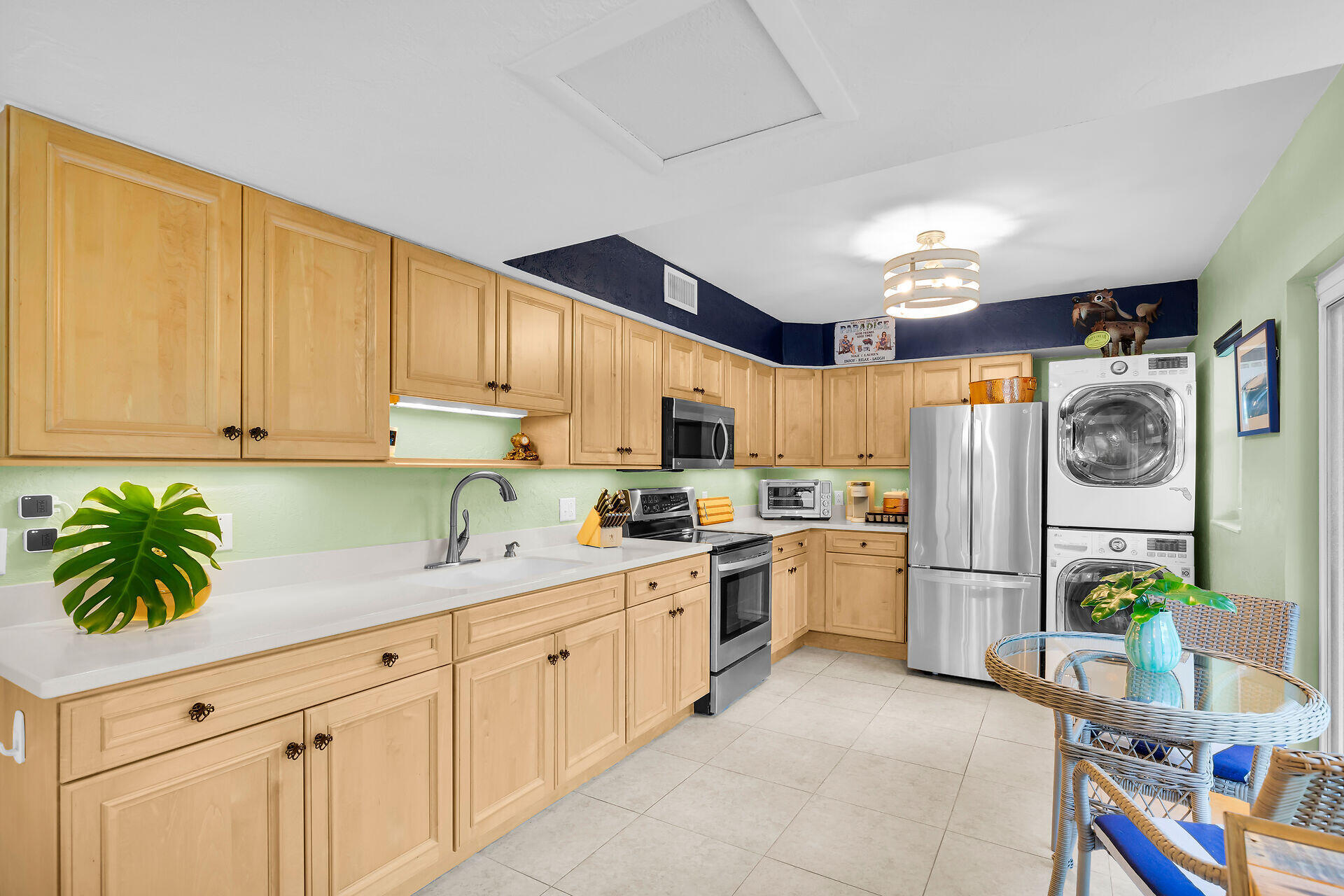 Kitchen with light wood cabinets, white counters, stainless steel appliances, and a stacked washer and dryer.