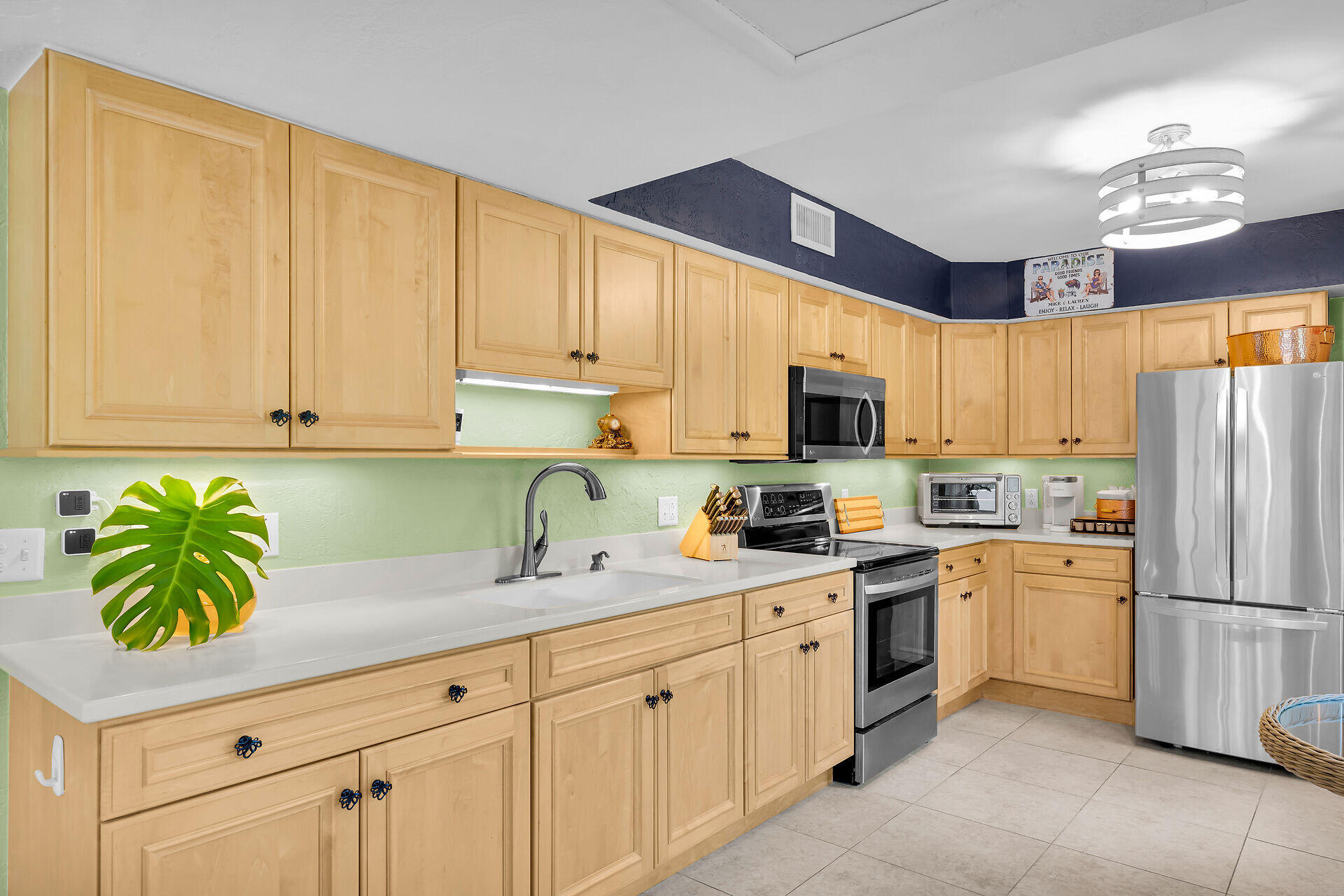 Kitchen with honey-colored cabinets, pale green walls, white counters, and stainless steel appliances.