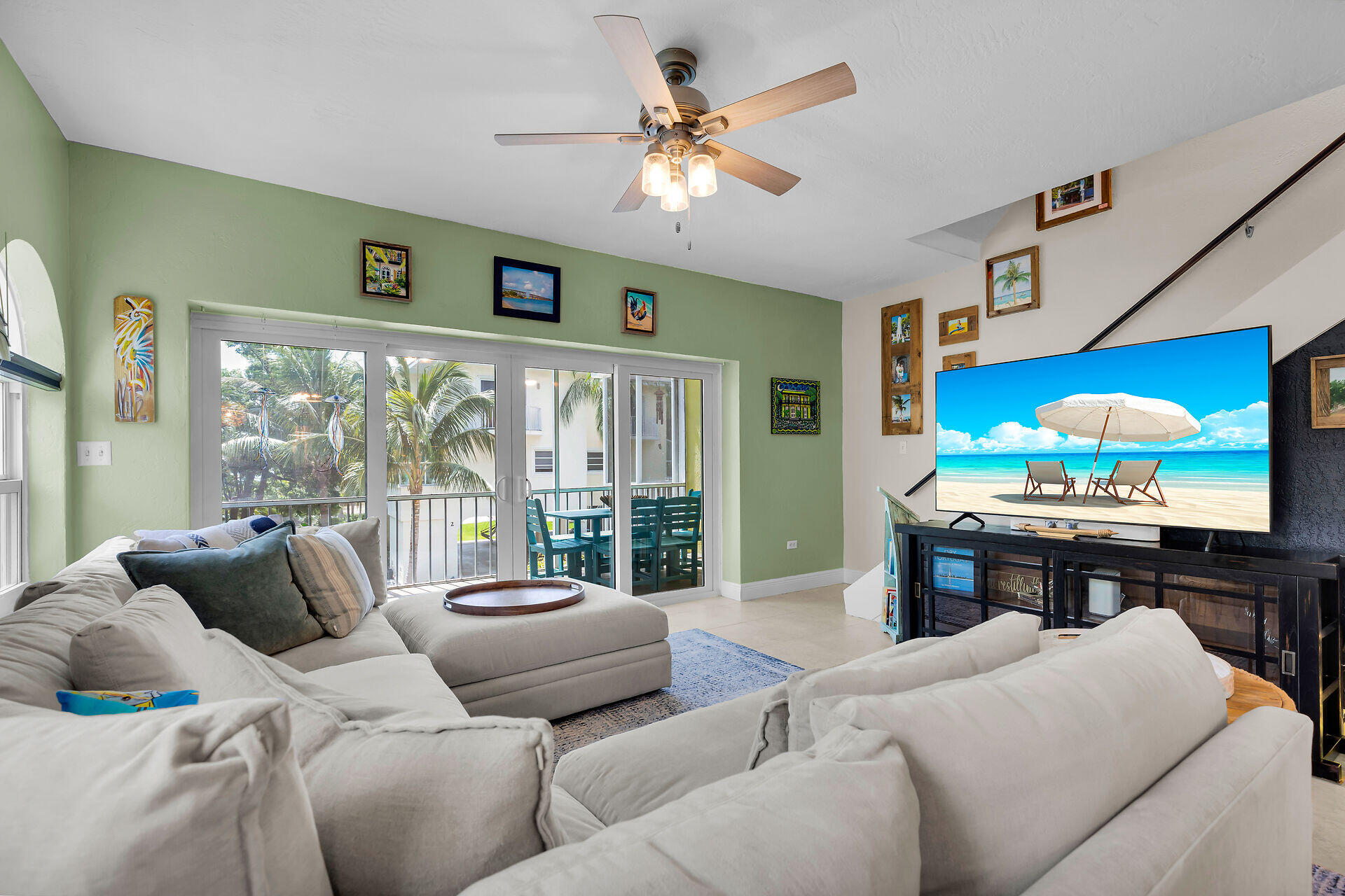 Living room with sage-green walls, sectional sofas, and sliding doors opening onto a tropical balcony.