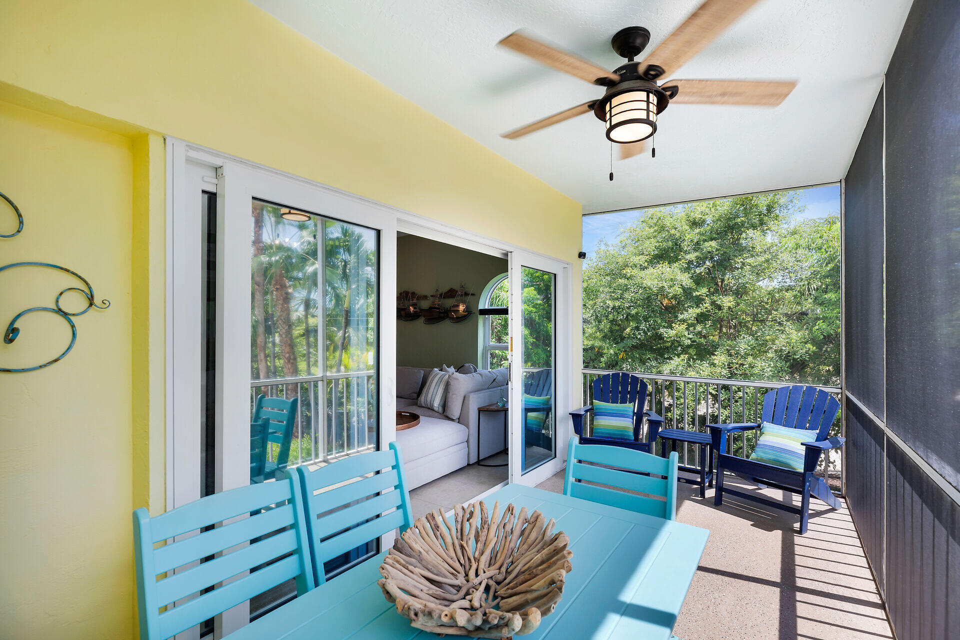 Covered balcony with turquoise dining furniture and blue chairs overlooking leafy trees.