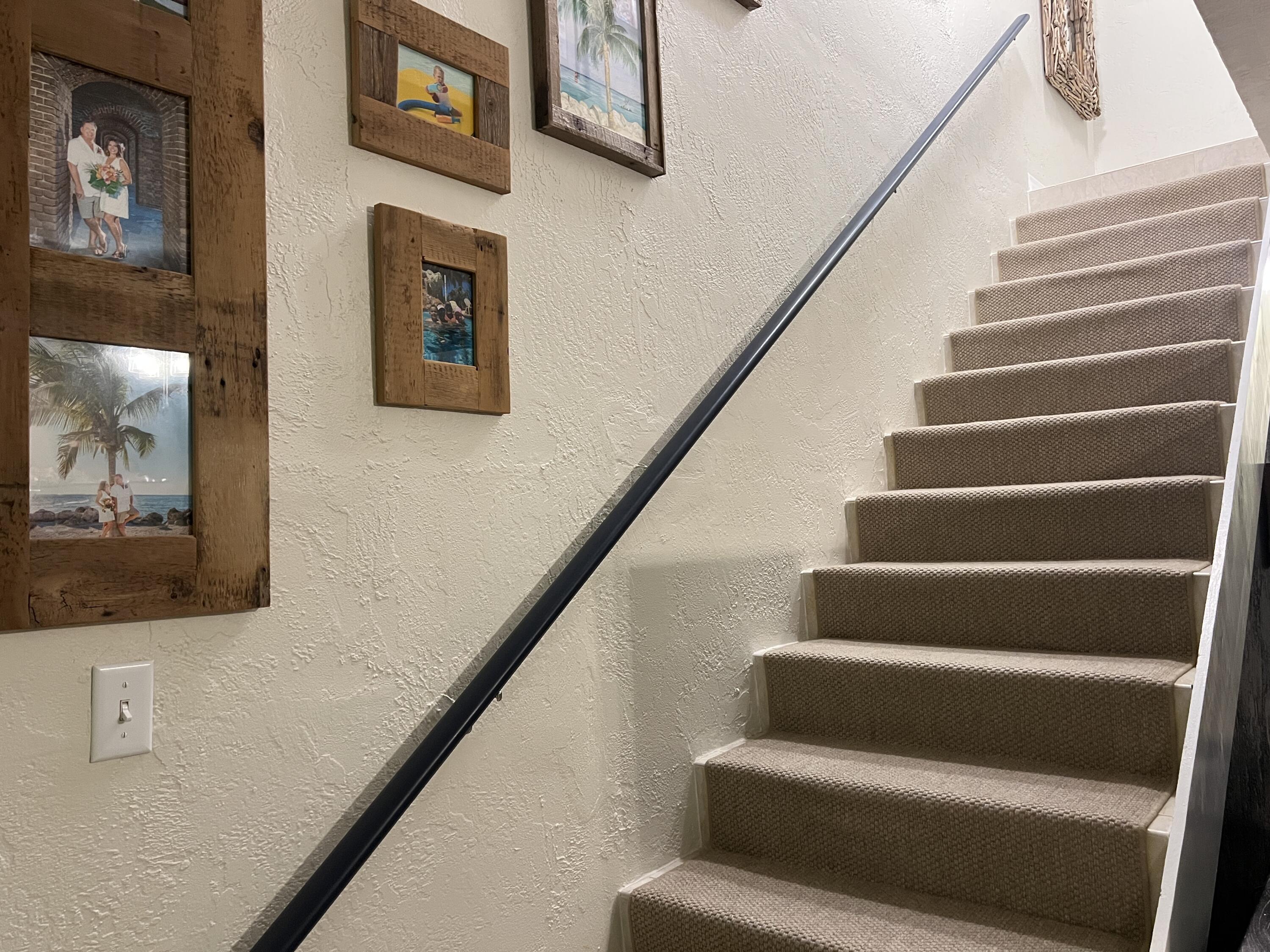 Carpeted staircase with a black handrail and rustic framed family and beach photos on the wall.