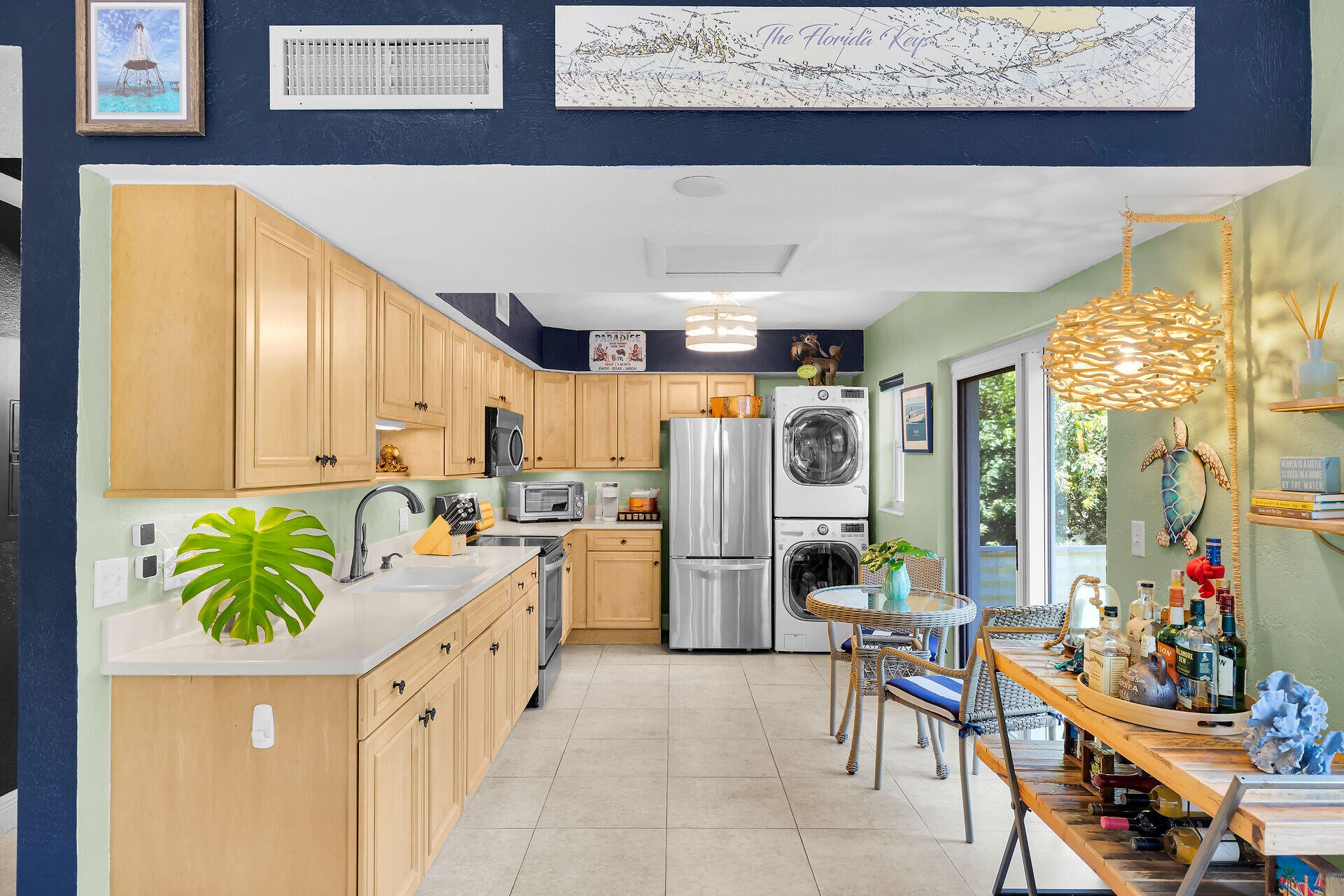 Kitchen with light wood cabinets, stainless steel appliances, stacked washer and dryer, and a wicker dining nook.