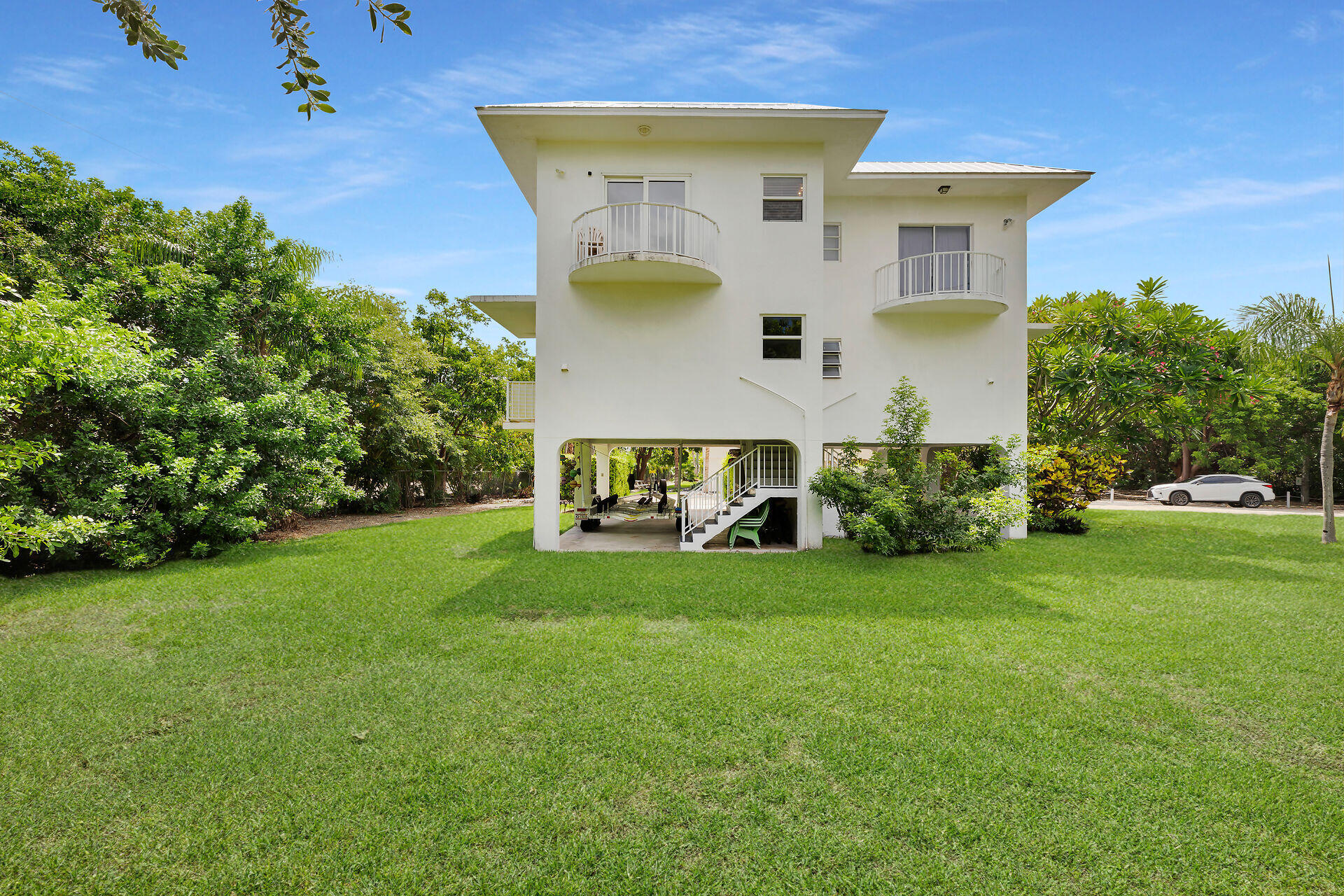 White elevated home with two balconies and a broad lawn bordered by tropical landscaping.
