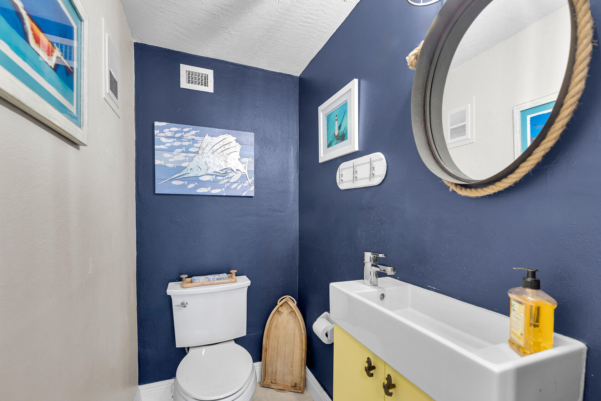 Bathroom with navy walls, a white sink and toilet, yellow vanity doors, and a rope-framed mirror.