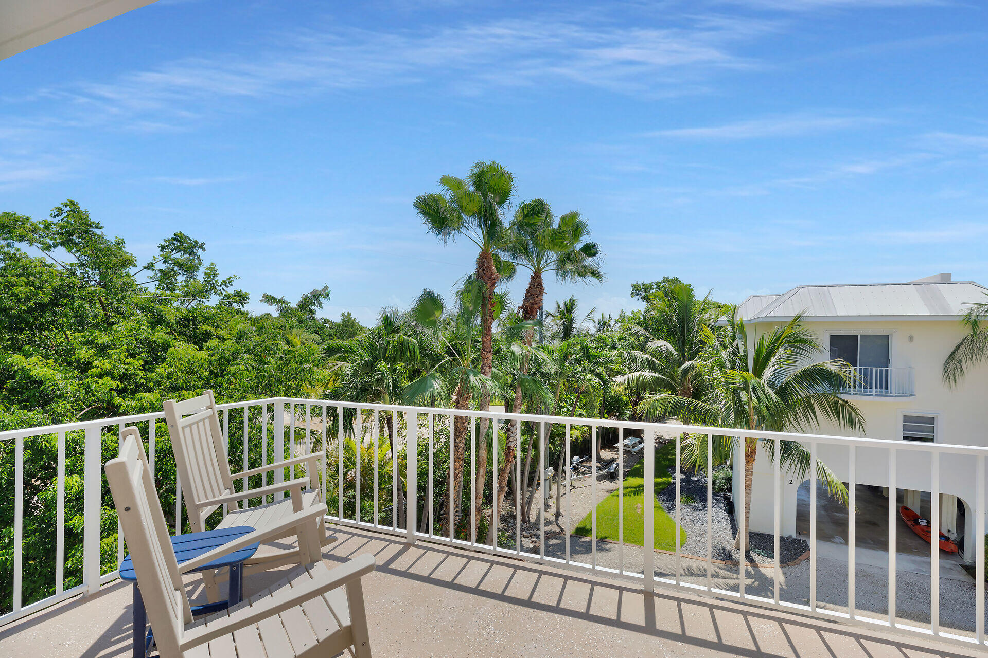 Furnished balcony overlooking tropical palms and a neighboring white building.