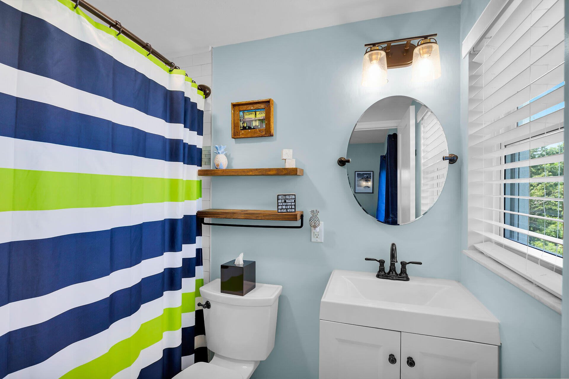 Bathroom with pale blue walls, a white vanity, and a bold navy, white, and lime-green striped shower curtain.