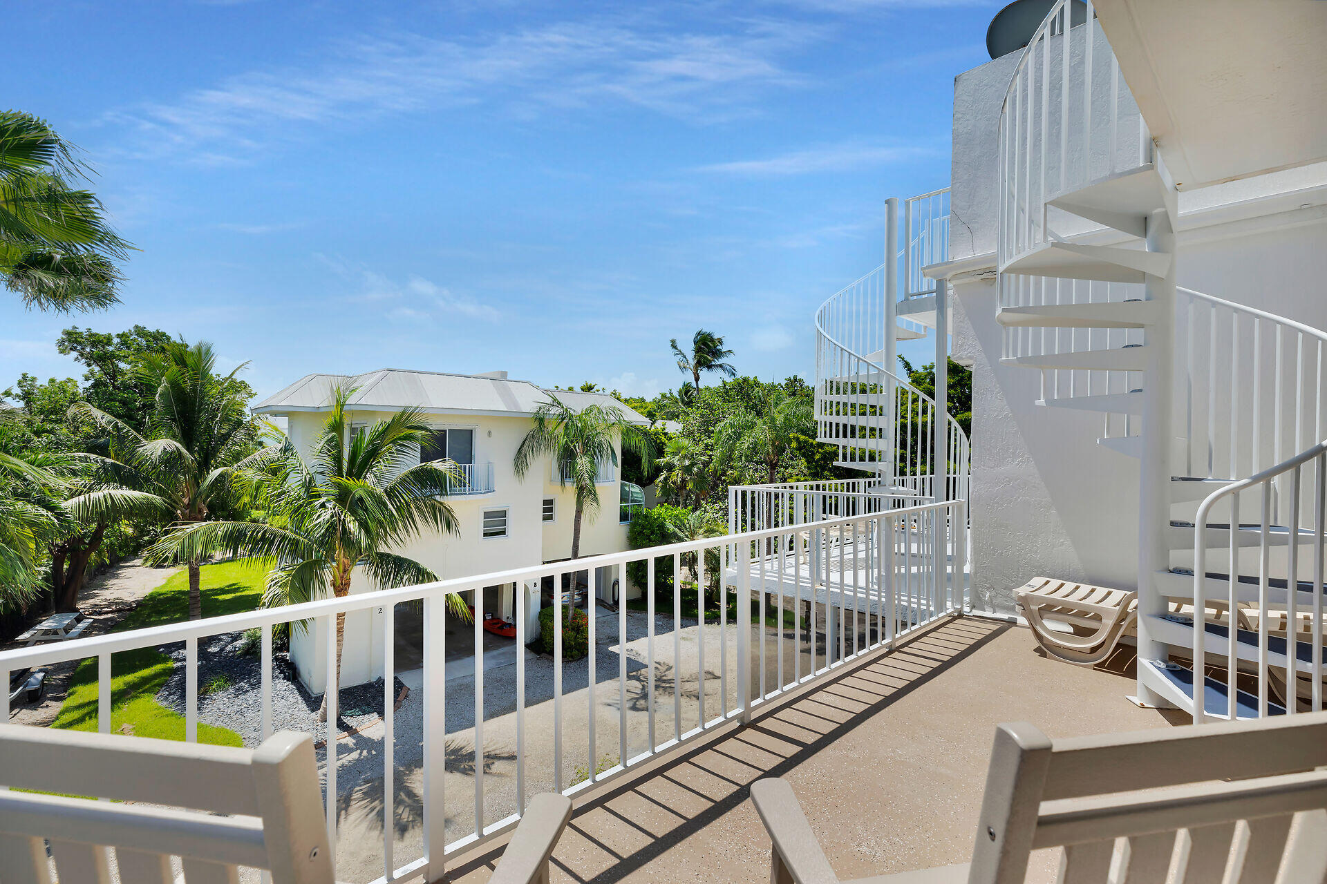 Upper-level balcony with a white spiral staircase overlooking palm trees and a neighboring home.