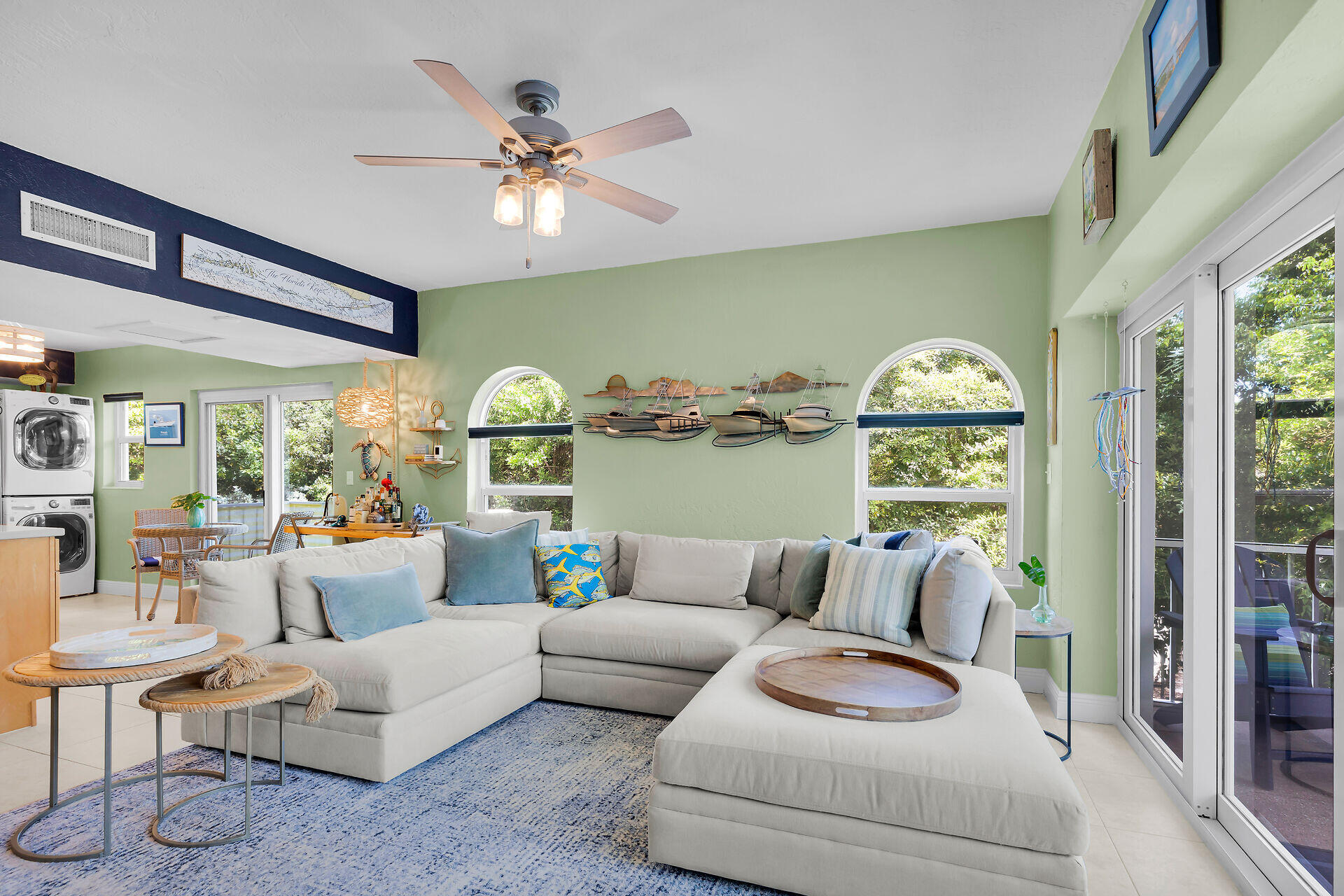 Living room with a white sectional, nautical boat models, arched windows, and sliding glass doors.