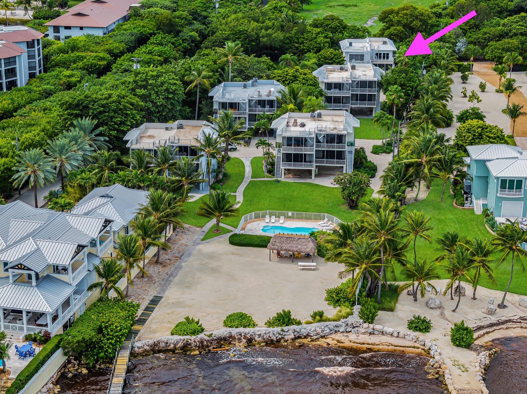 Aerial waterfront residences with a magenta arrow marking one building beside the beach and pool.