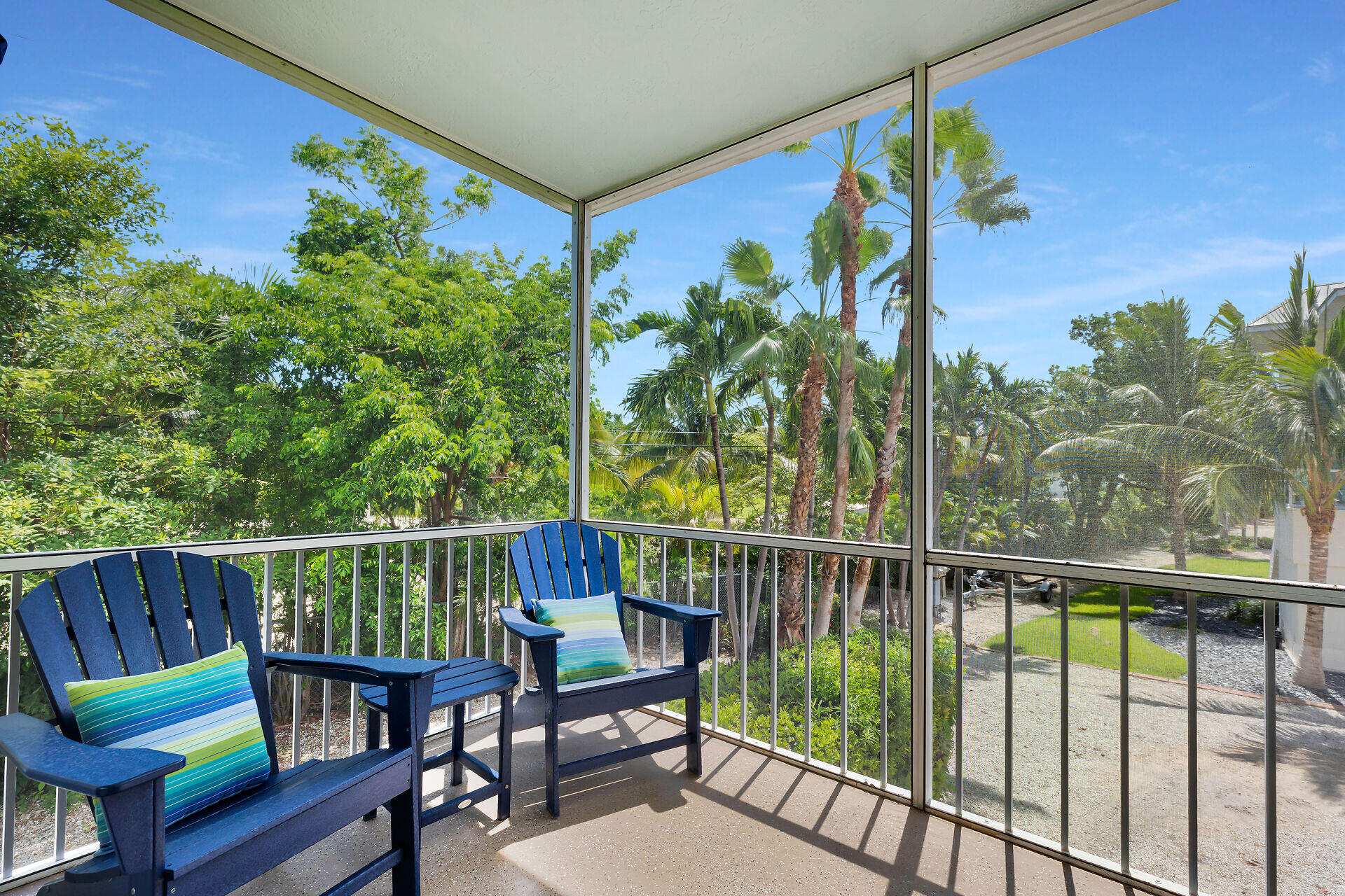 Screened balcony with blue Adirondack chairs overlooking tropical palms and greenery.