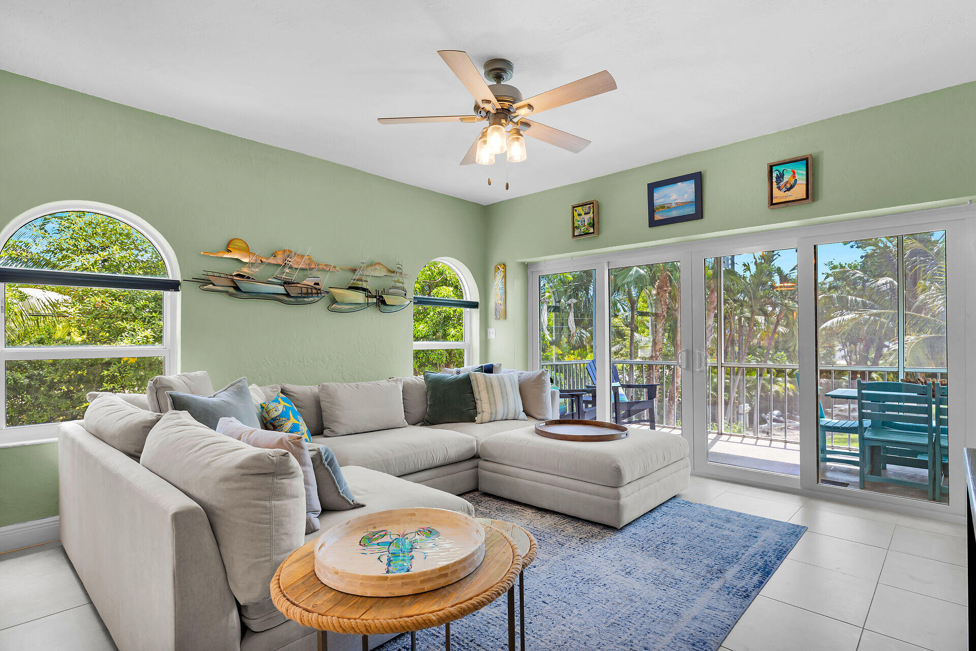Living room with a large sectional, arched windows, and sliding doors overlooking tropical greenery.