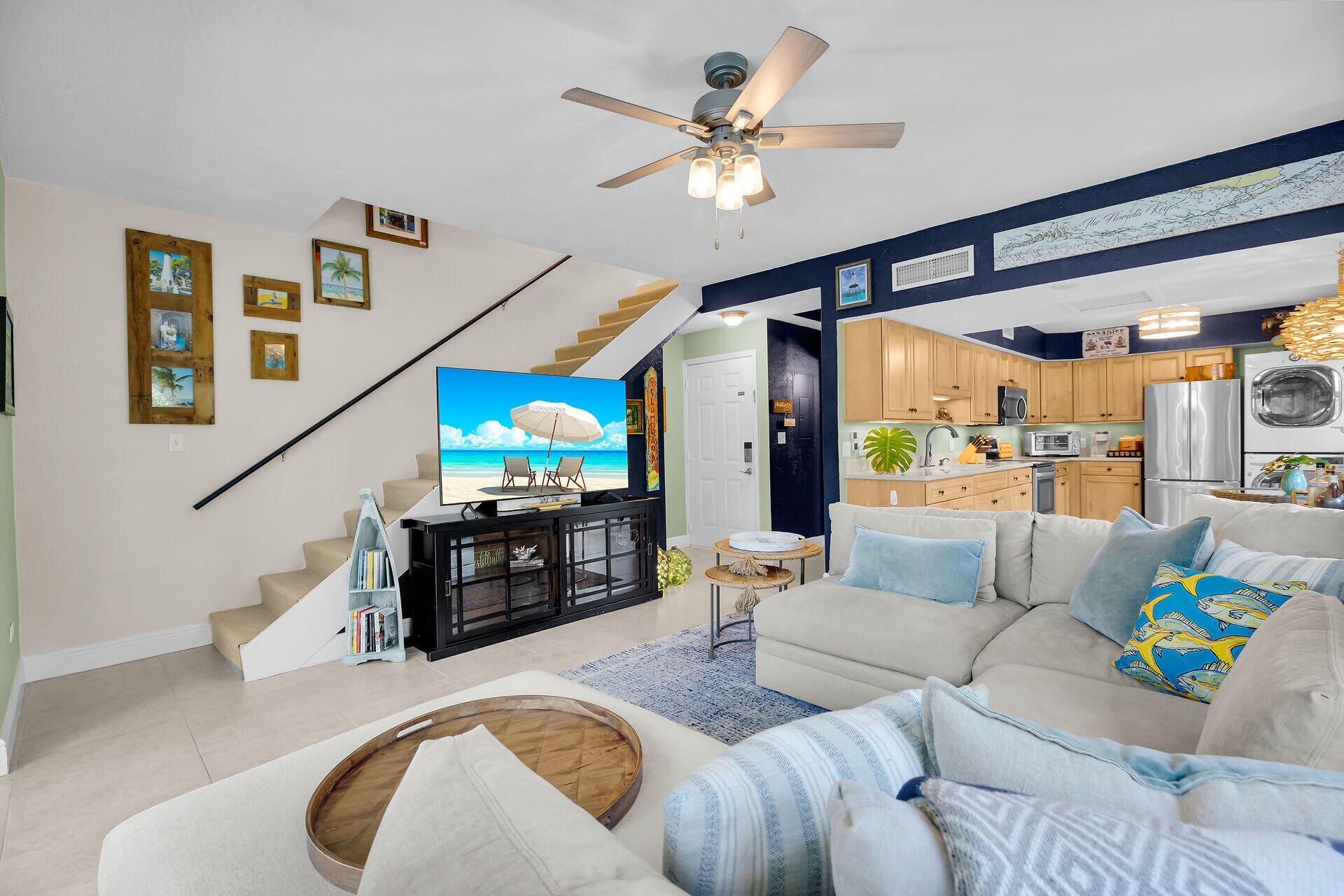 Open living room and kitchen with a staircase, light wood cabinets, and a gray sectional sofa.
