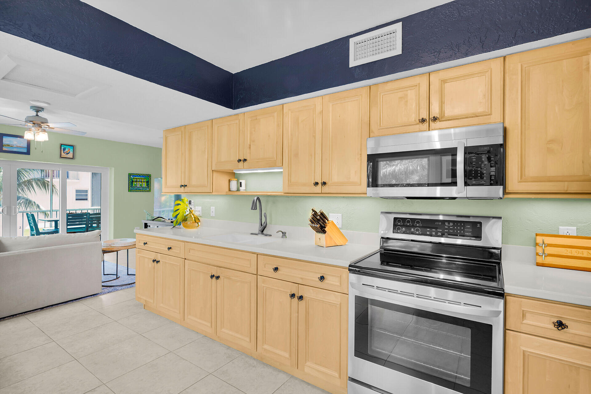 Kitchen with light wood cabinets, white counters, and stainless steel appliances beside a sliding glass door.
