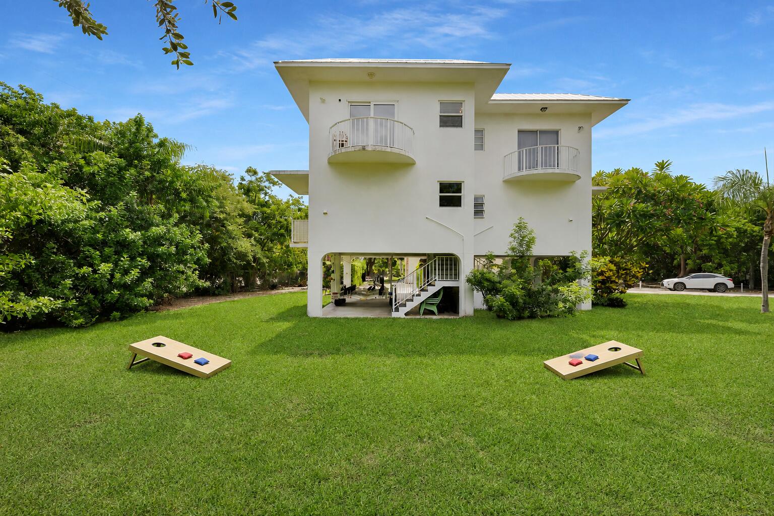 White two-story home with curved balconies, open ground level, and cornhole boards on the lawn.