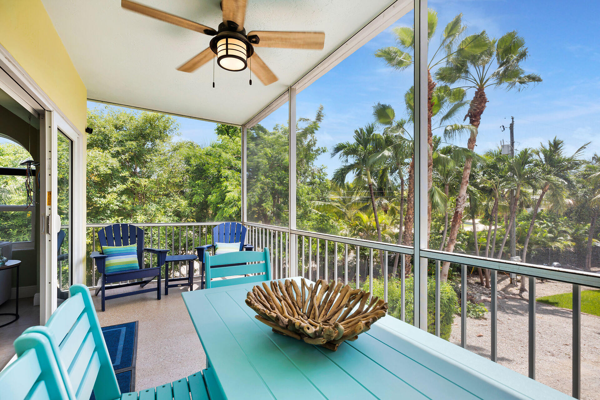 Screened porch with turquoise dining set and blue chairs overlooking palm trees.