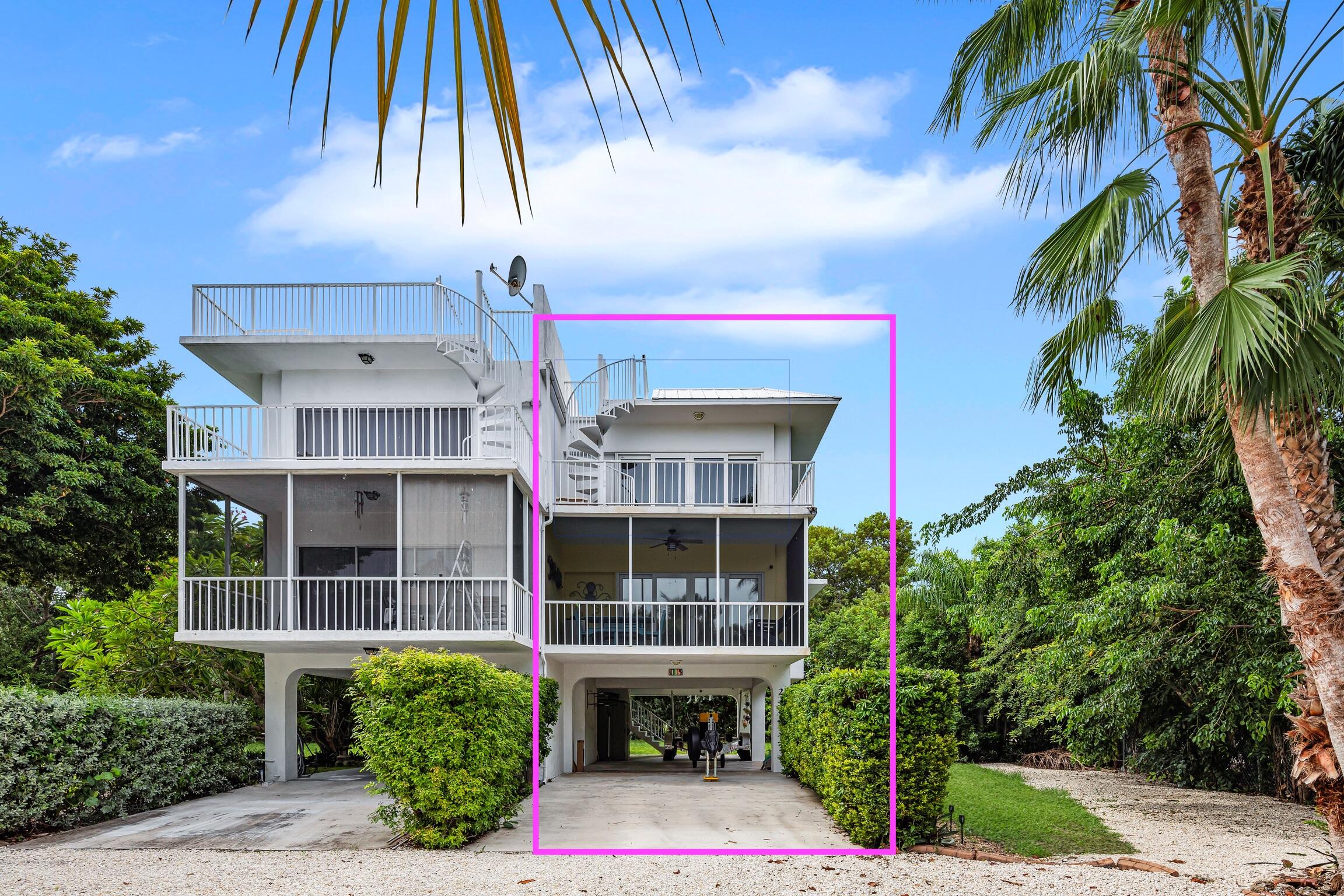 Elevated white home with stacked balconies and an exterior spiral staircase, surrounded by palms.
