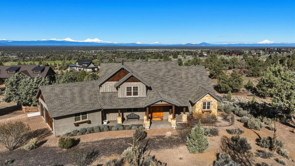 Aerial view of a ranch home with snow-capped mountains across the horizon.