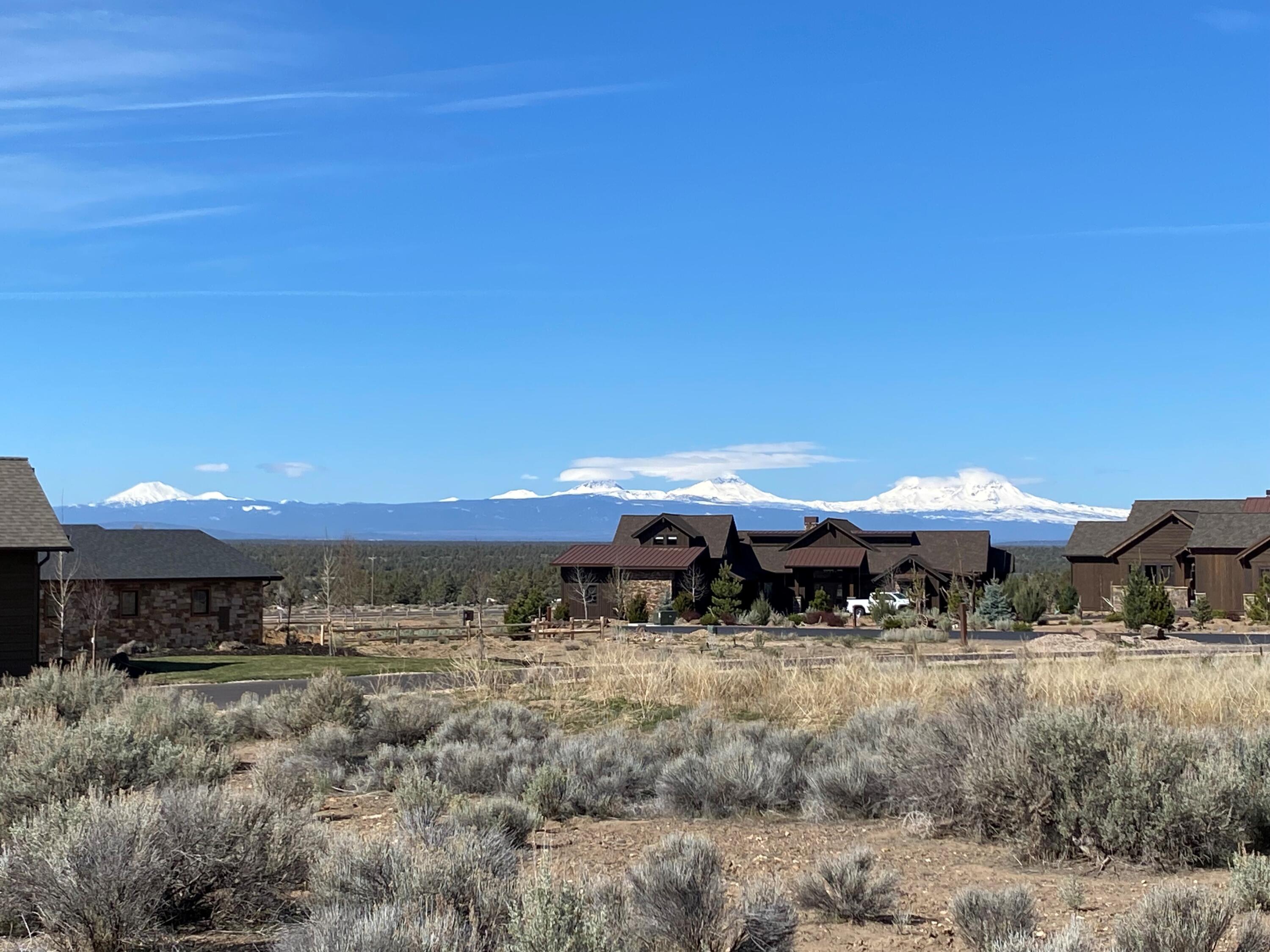 High-desert homesite with sagebrush, ranch-style homes, and snow-covered mountains in the distance.