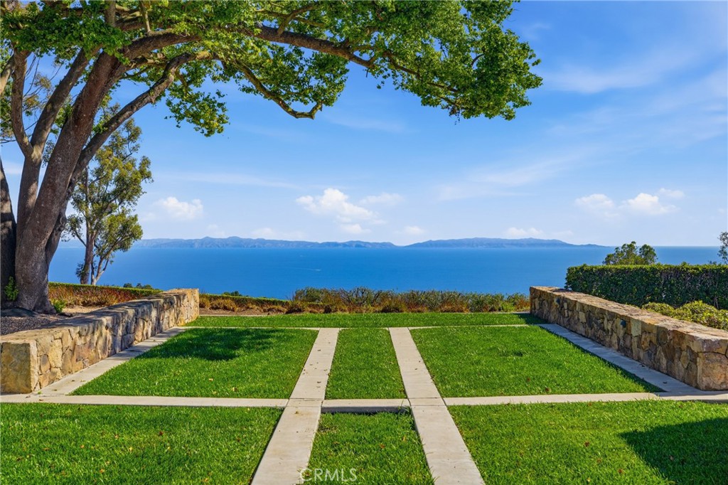 Ocean view across a landscaped lawn with stone walls and a mature shade tree.