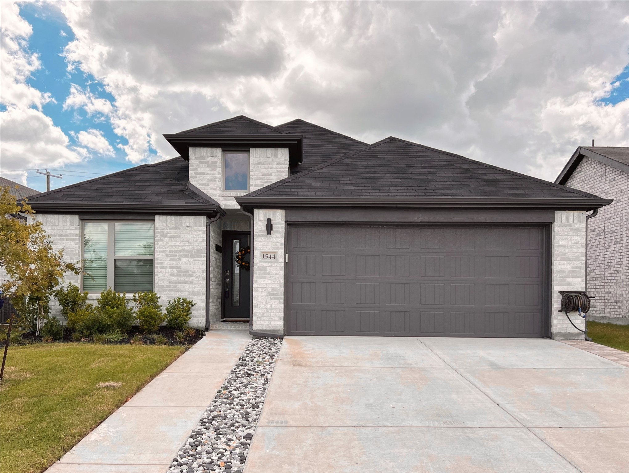 Light-brick home with dark roof, wide two-car garage, and landscaped driveway.