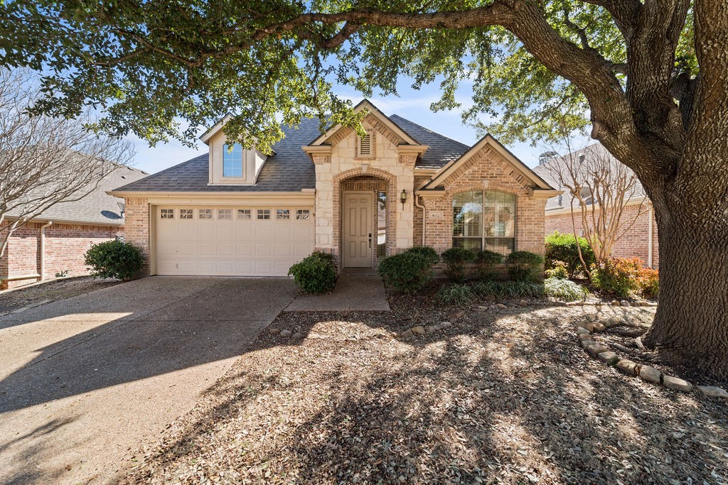 Brick and stone house with a two-car garage beneath a large shade tree.