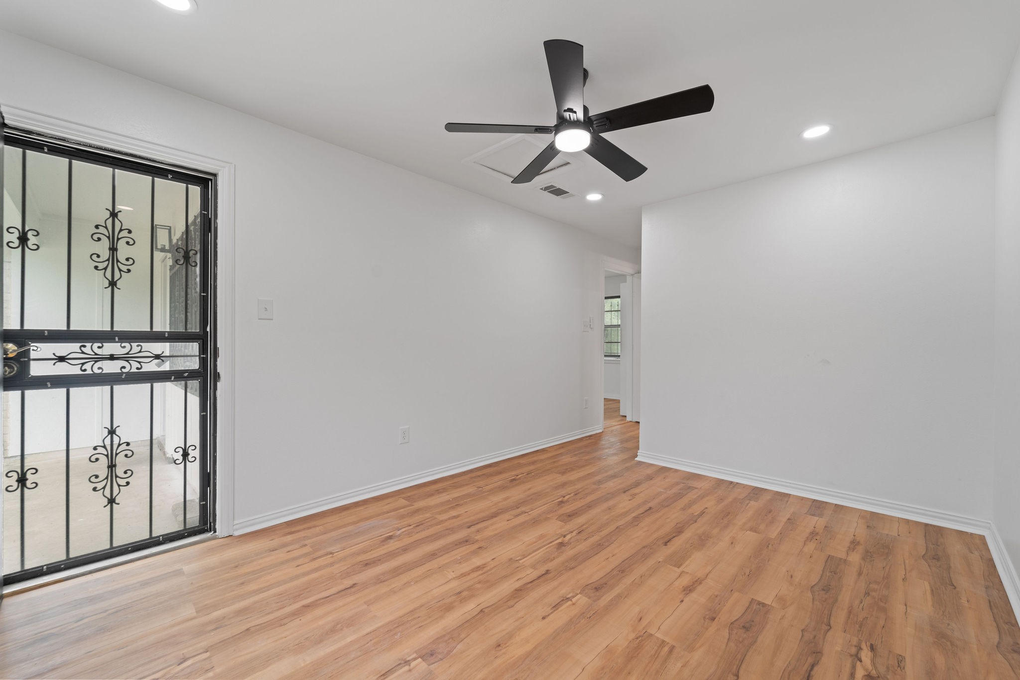Empty room with warm wood flooring, a black ceiling fan, and a decorative security door.