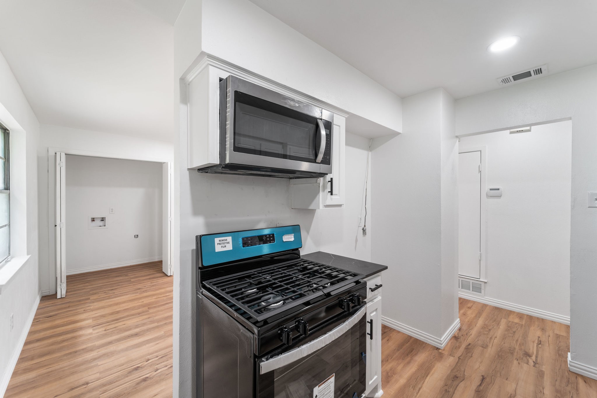 Vacant kitchen with a stainless-steel gas range, over-the-range microwave, and warm wood-look flooring.