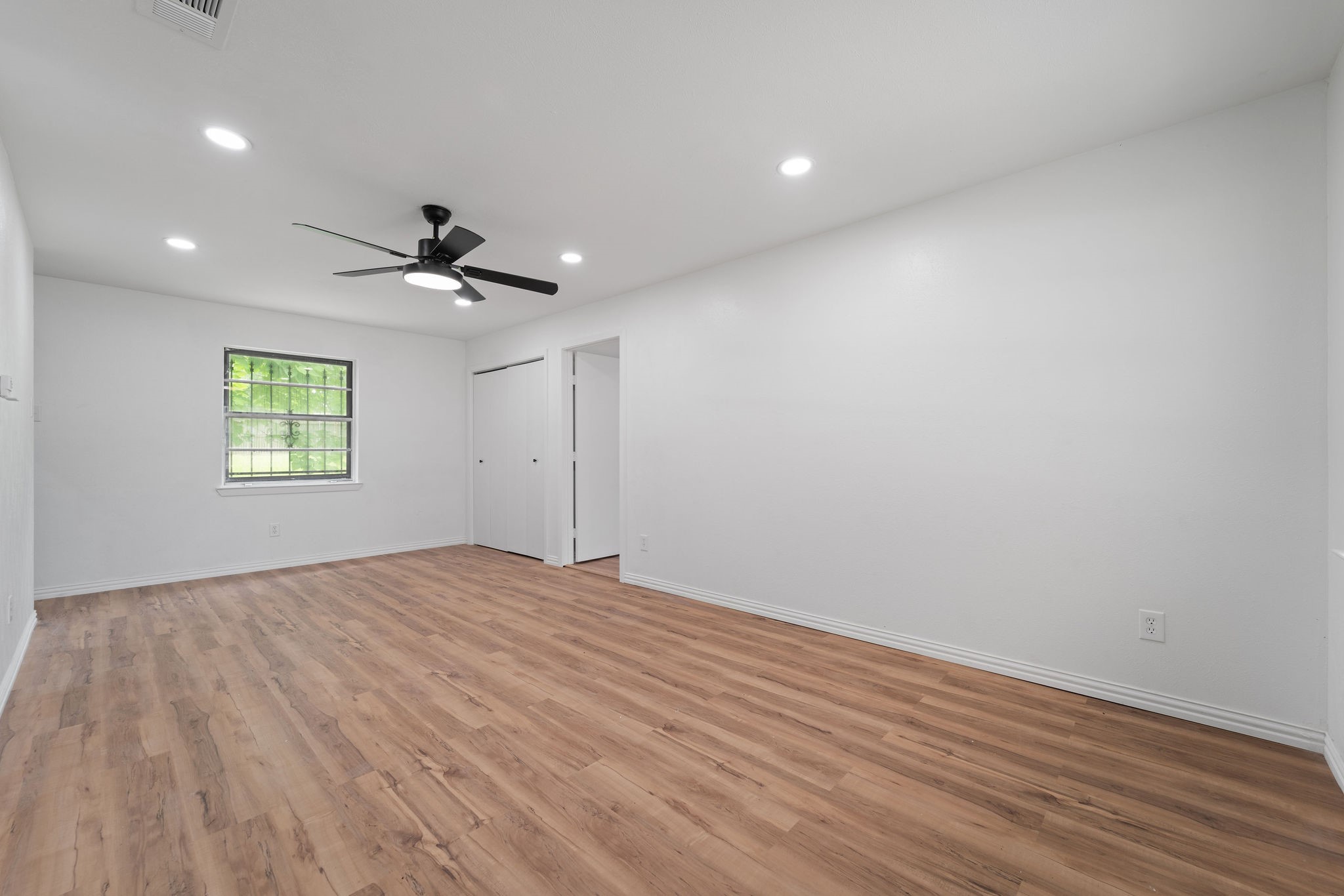 Empty bedroom with wood-look flooring, a window, closet, and black ceiling fan.