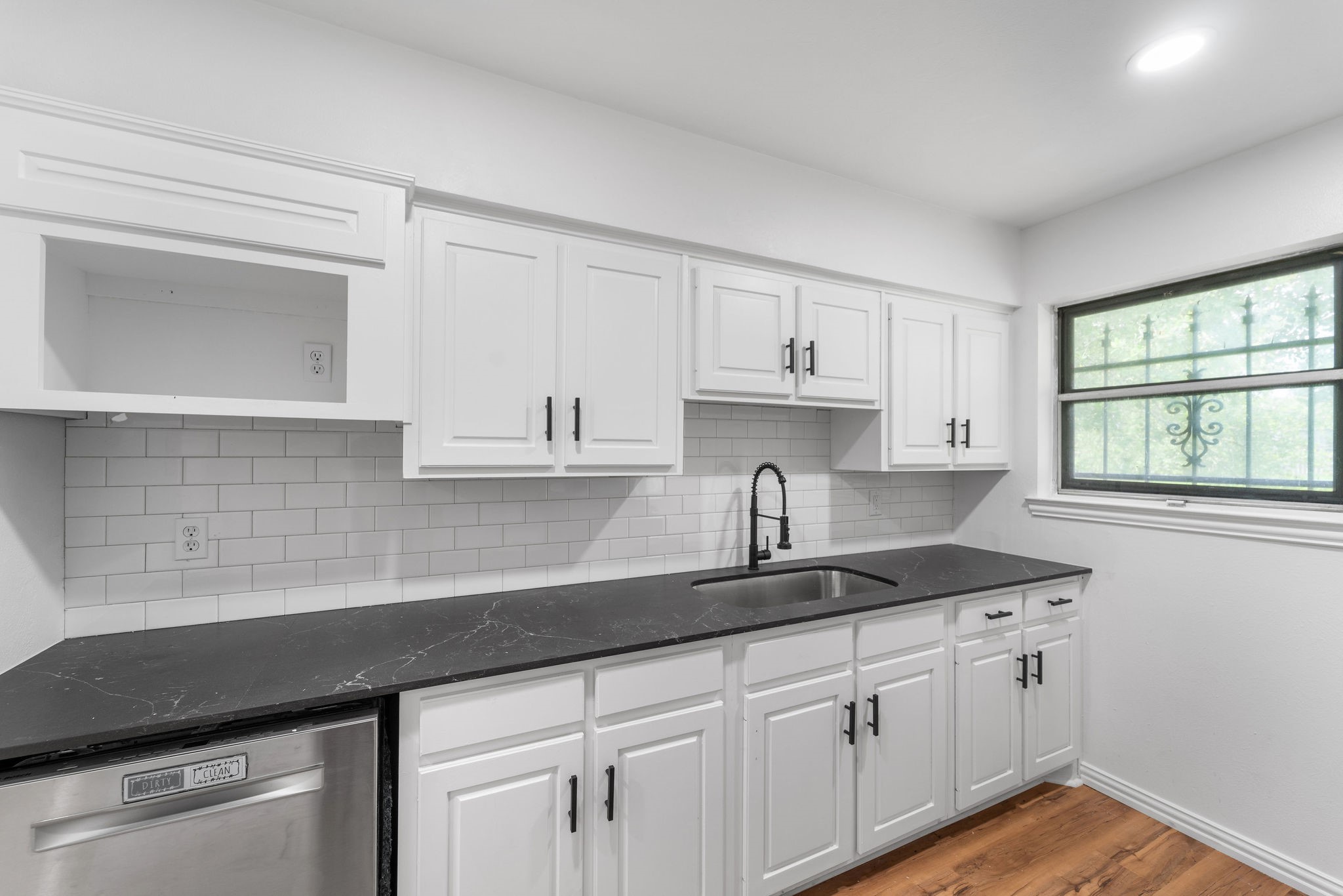 Kitchen with white cabinets, dark countertops, subway-tile backsplash, and a window with decorative ironwork.