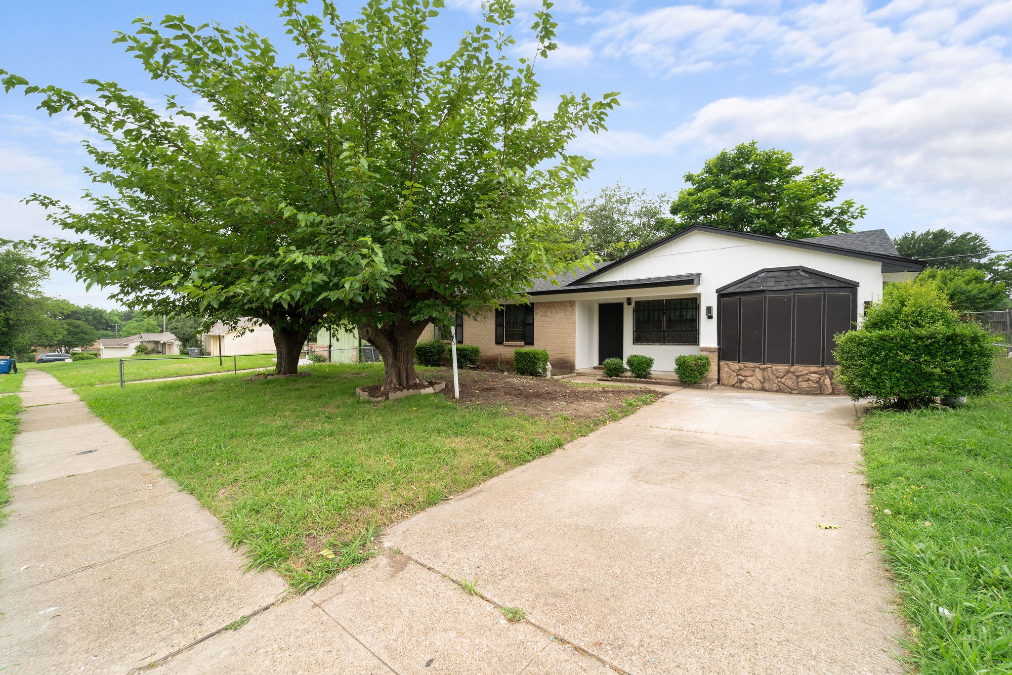 Single-story white and brick house with a broad driveway and mature trees across the front lawn.