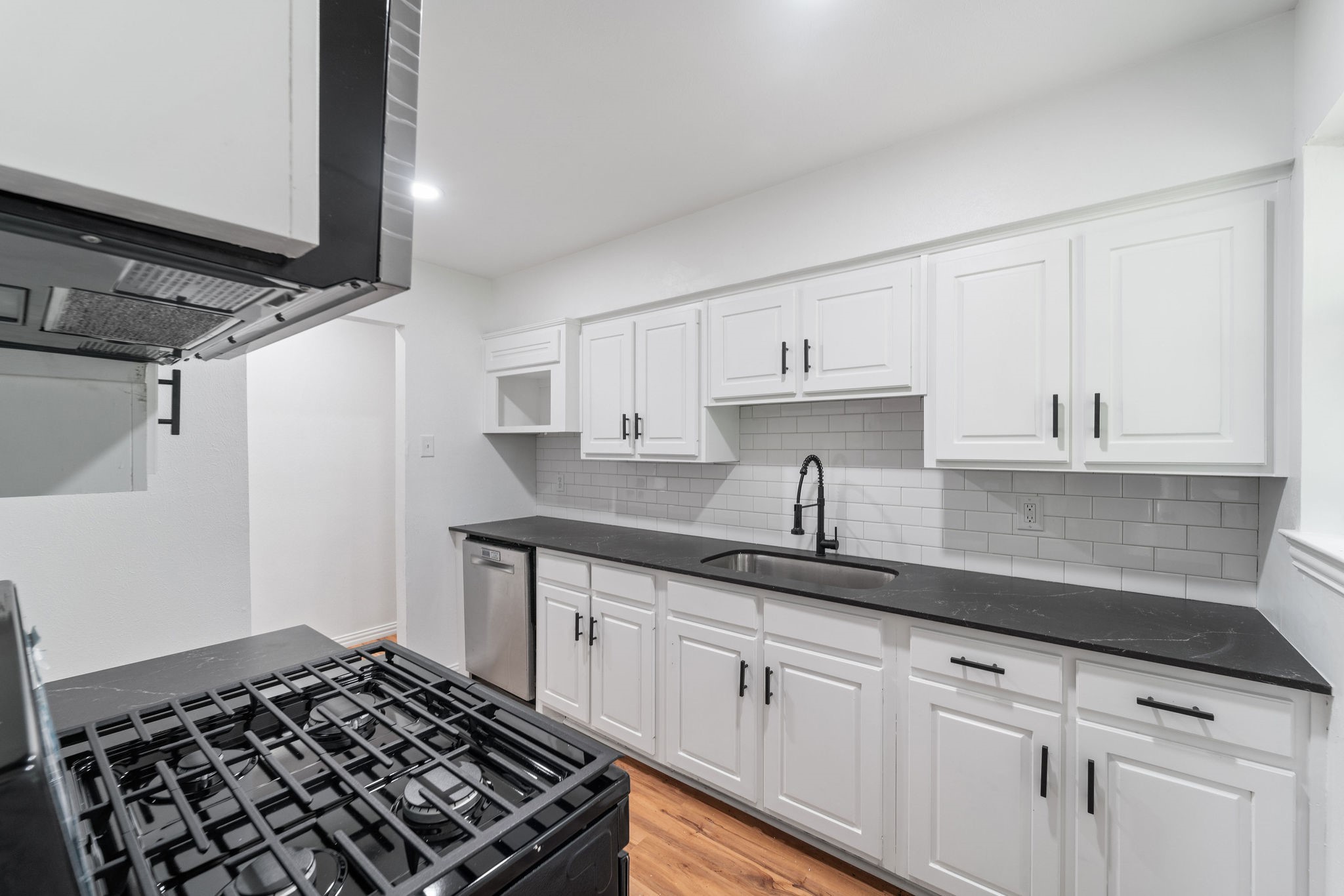 Kitchen with white shaker cabinets, dark countertops, subway tile backsplash, and a prominent black gas range.