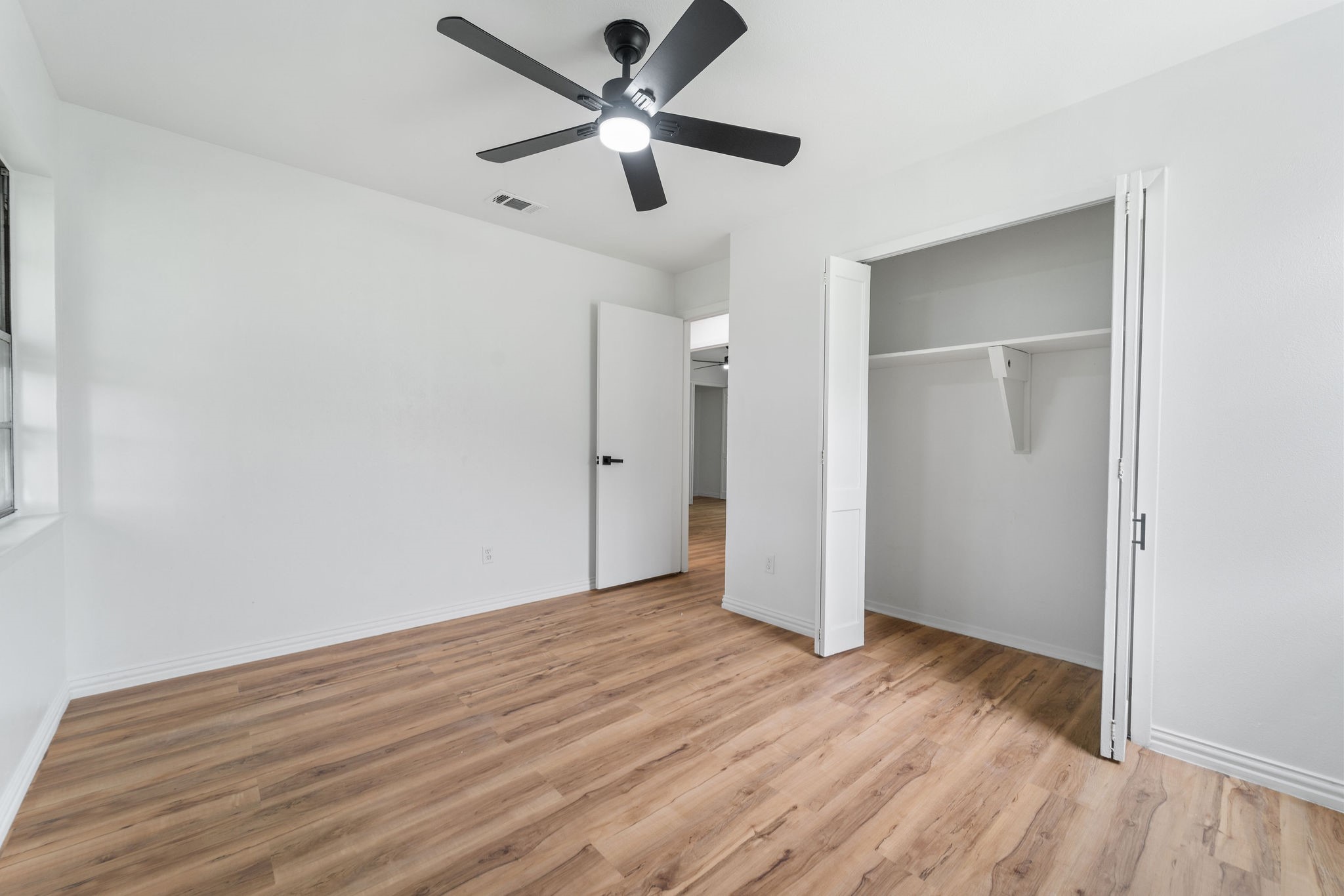 Empty bedroom with wood-look floors, a black ceiling fan, and an open closet.