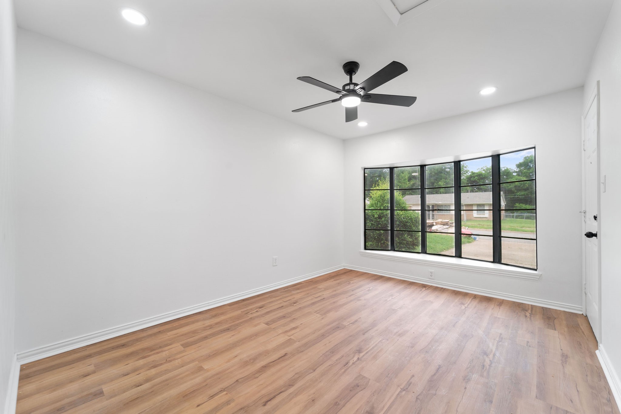 Empty room with wood flooring, large black-framed windows, and a ceiling fan.