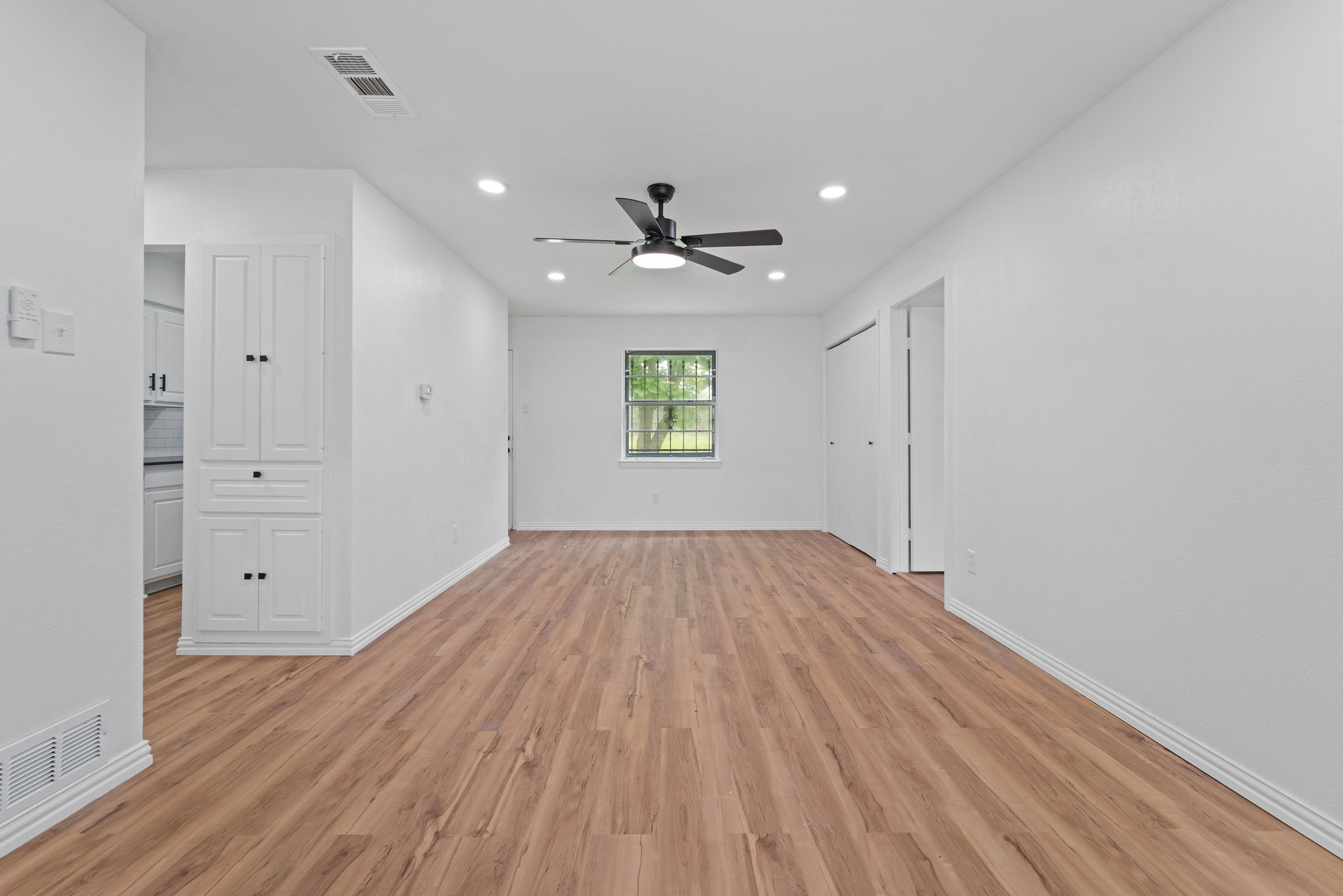 Empty living area with wood-look flooring, built-in cabinets, and a black ceiling fan.