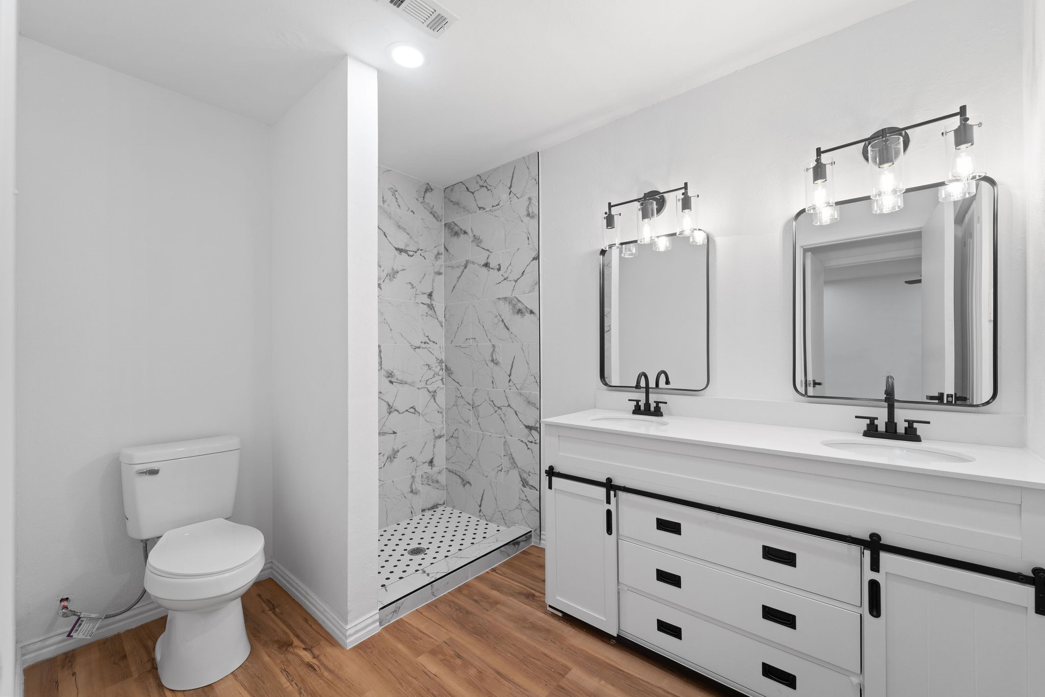Bathroom with a marble-tile shower and white double vanity with black fixtures.