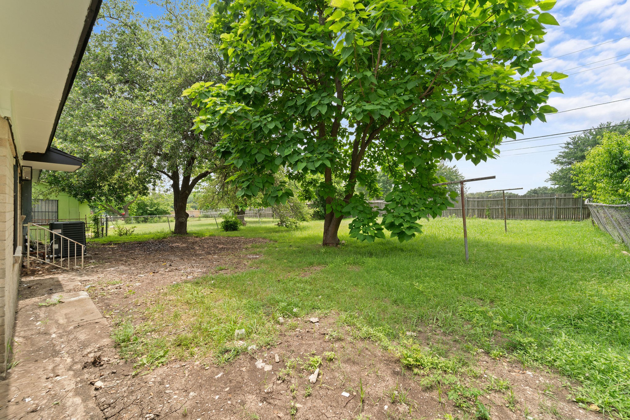 Grassy backyard with mature shade trees, a clothesline, and a wood privacy fence.