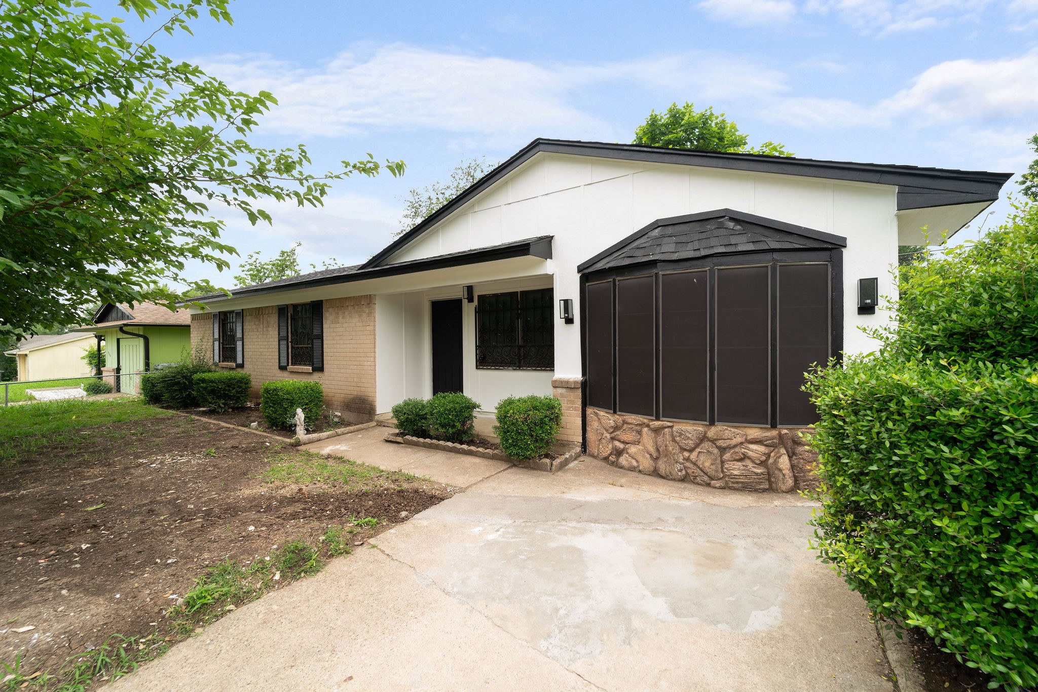 Single-story house with white siding, a brick facade, and a dark enclosed bay beside the concrete driveway.