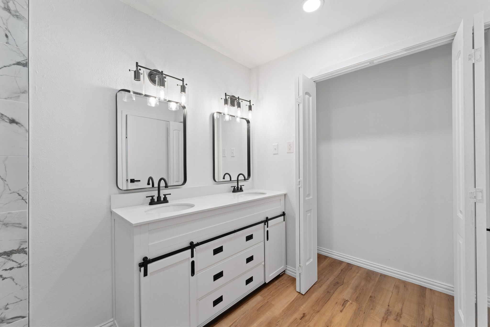 Bathroom with a double-sink white vanity, black fixtures, paired mirrors, and wood-look flooring.
