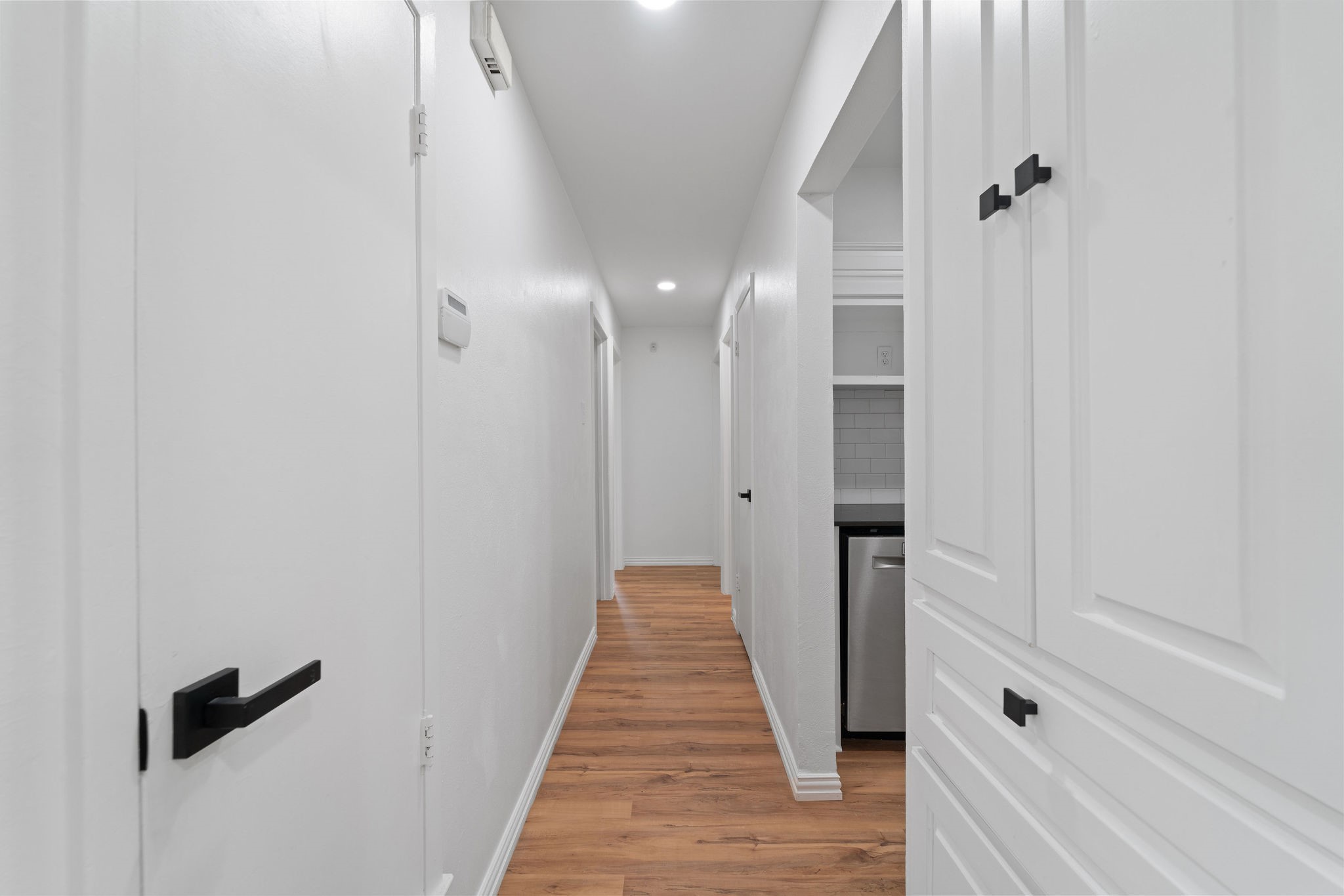 White hallway with warm wood floors and a glimpse of the kitchen.