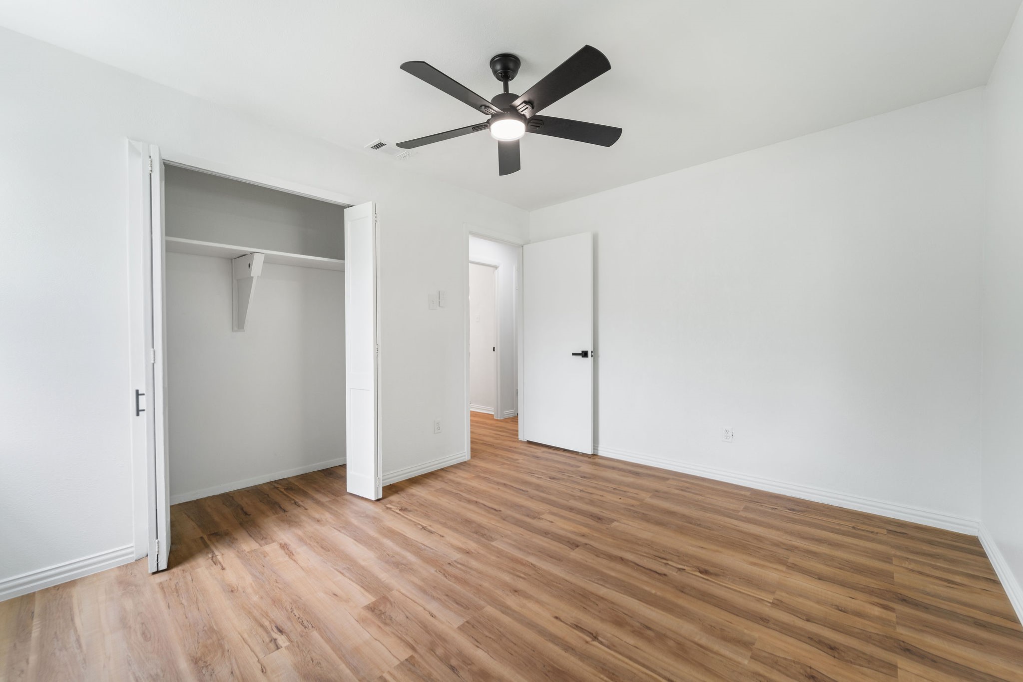Empty bedroom with wood-look flooring, an open closet, and a black ceiling fan.